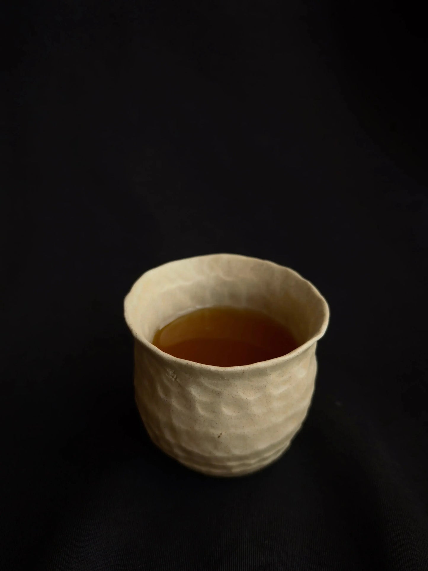 Handcrafted ceramic cup with textured surface, filled with tea, on a black background