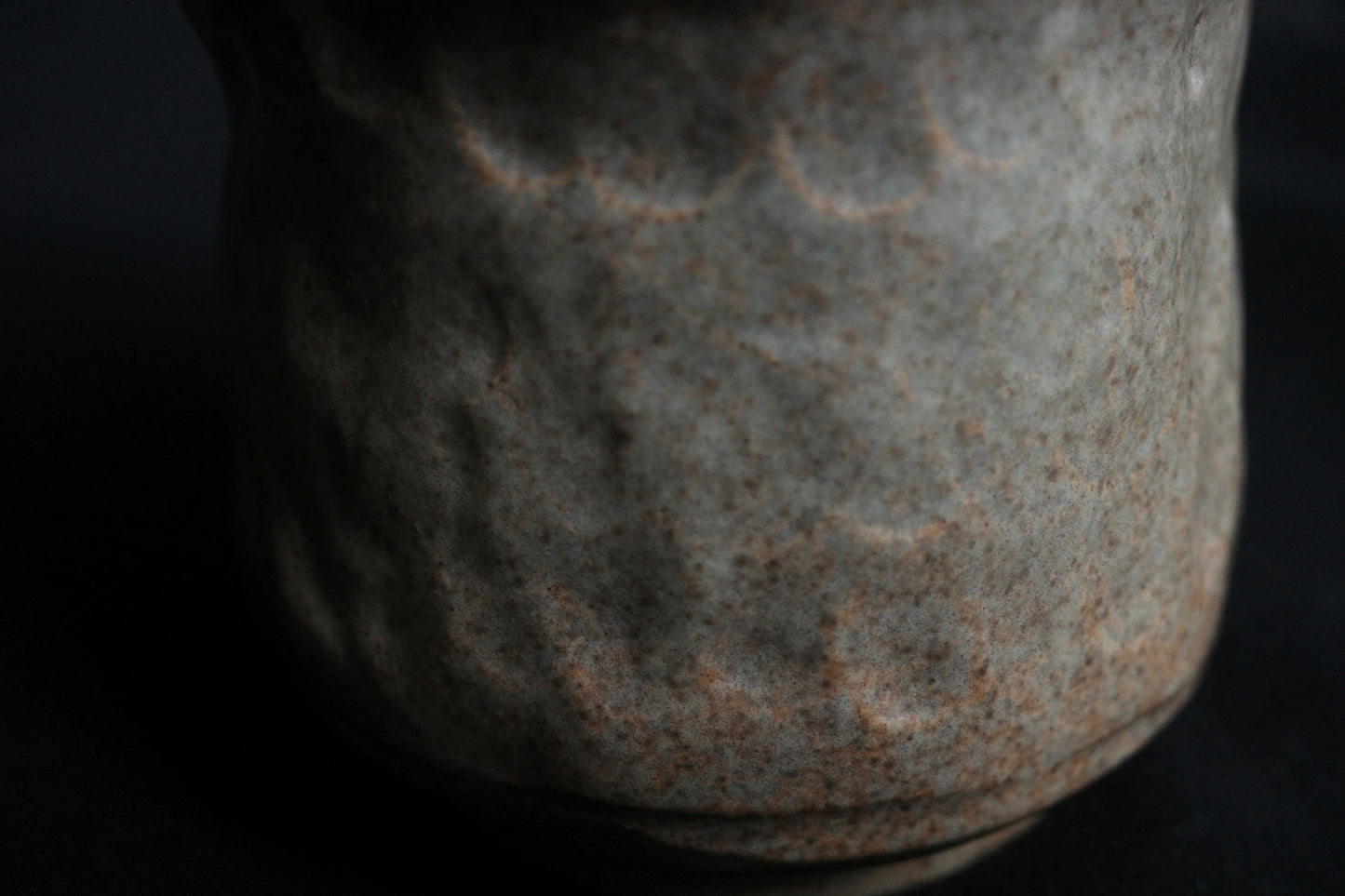 Close-up of handcrafted ceramic vase with textured, speckled gray and brown surface
