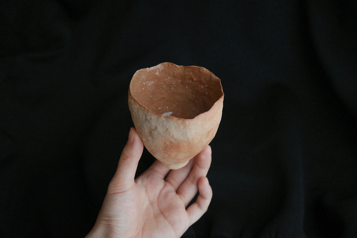 Hand holding a handcrafted, minimalist ceramic cup with organic texture against a black background