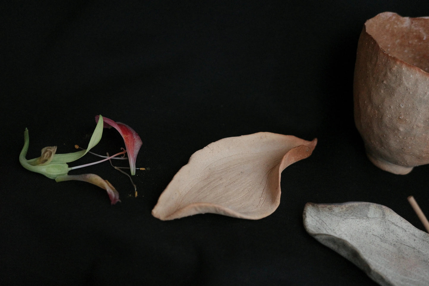 Handcrafted ceramic bowl and leaf-shaped dish with flower petals on black background