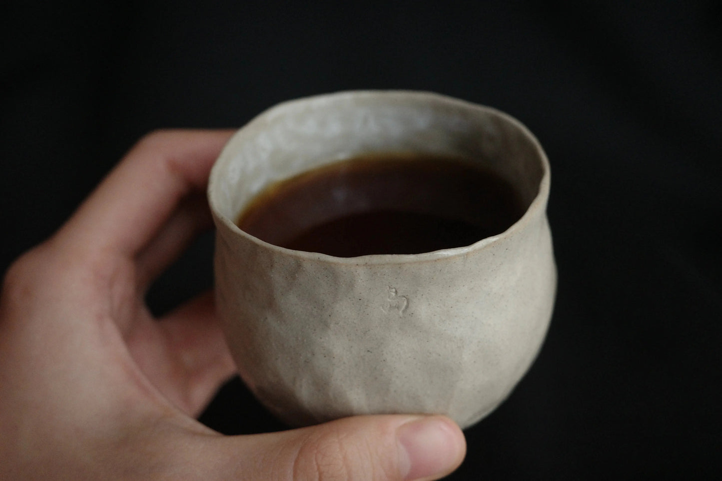 Hand holding a handcrafted ceramic cup with coffee, minimal and textured design