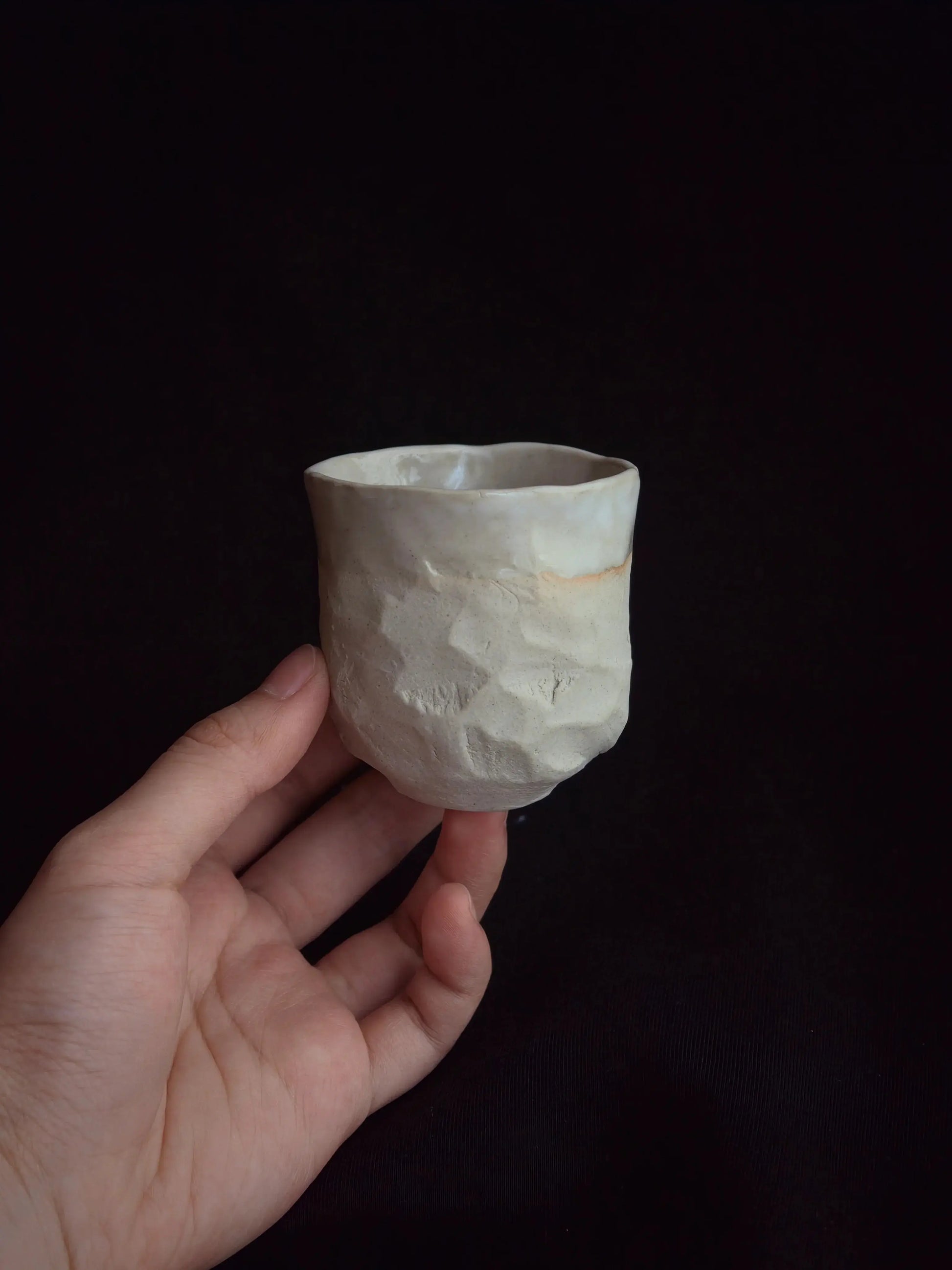 Hand holding a handcrafted ceramic cup with a textured, minimalist design against black background