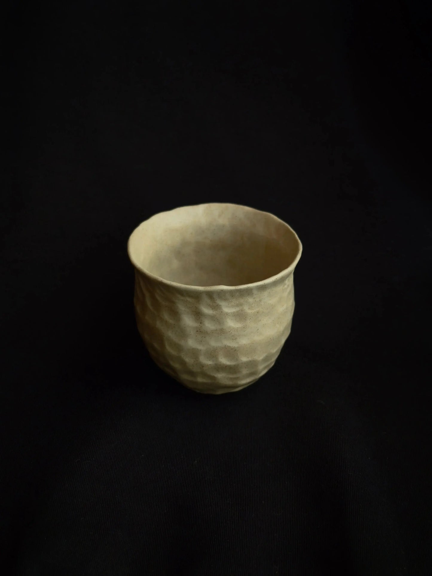 Minimalist handcrafted ceramic cup with textured surface on black background