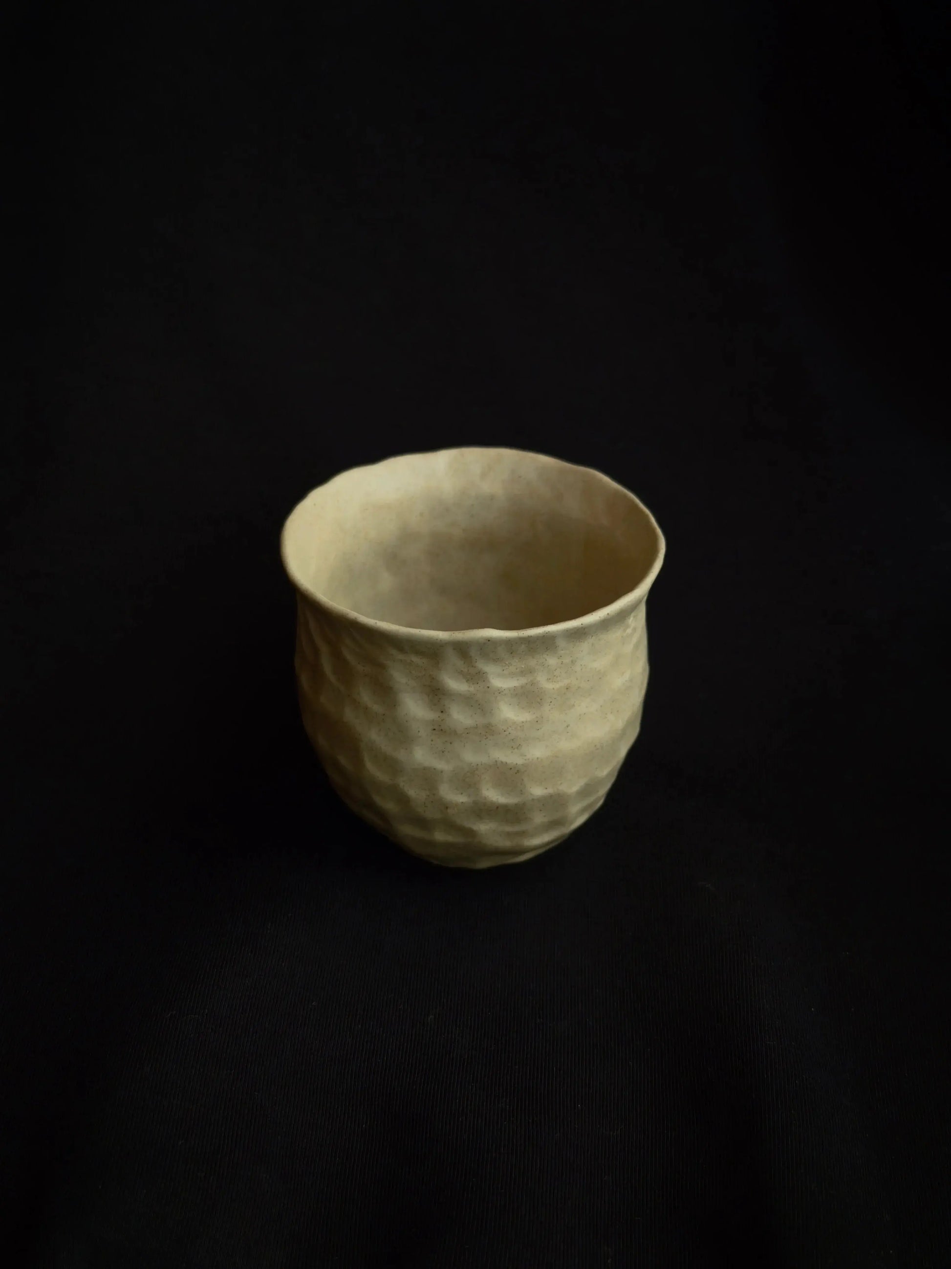 Minimalist handcrafted ceramic cup with textured surface on black background