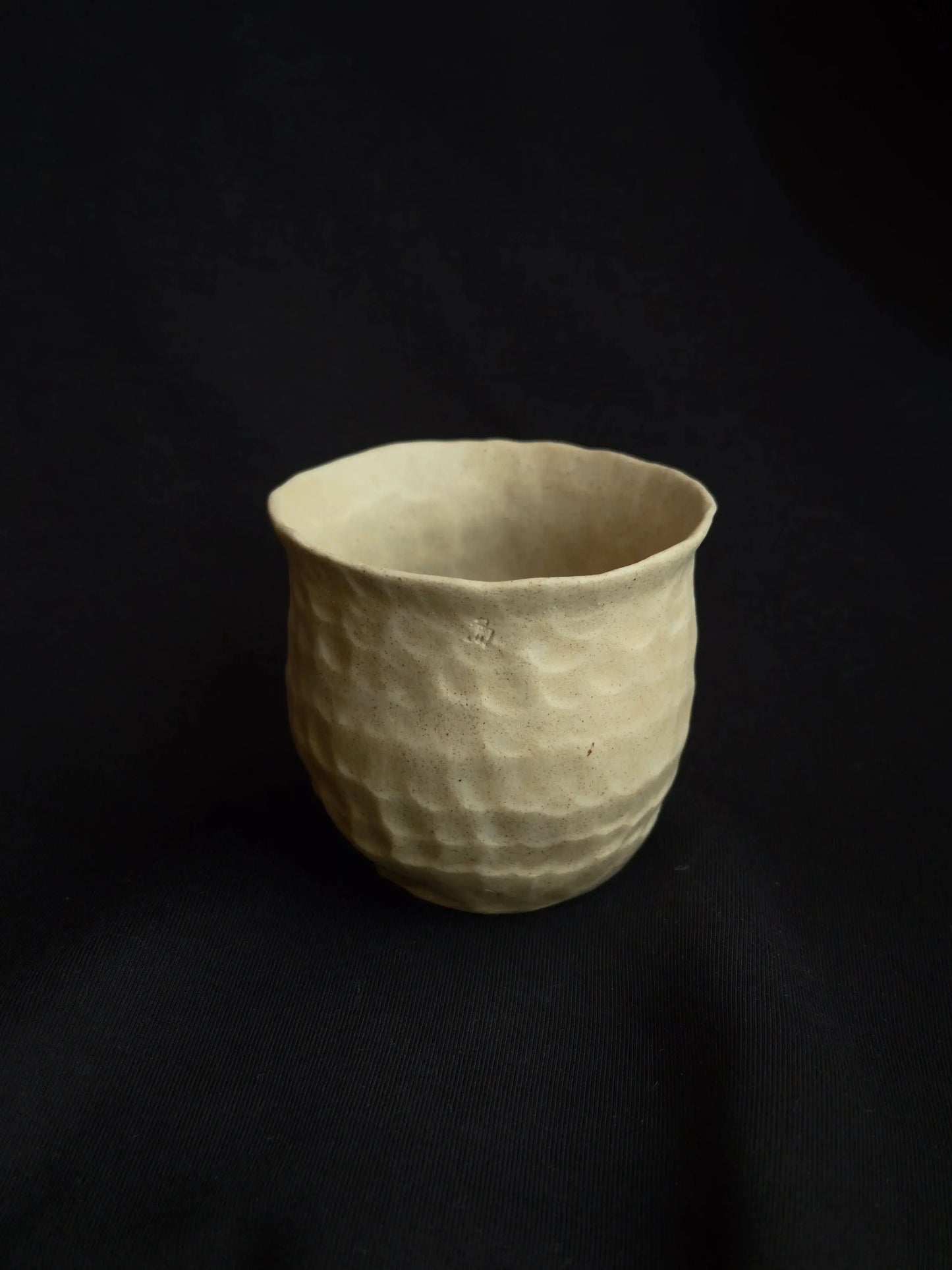 Handcrafted beige ceramic cup with textured surface on a black background