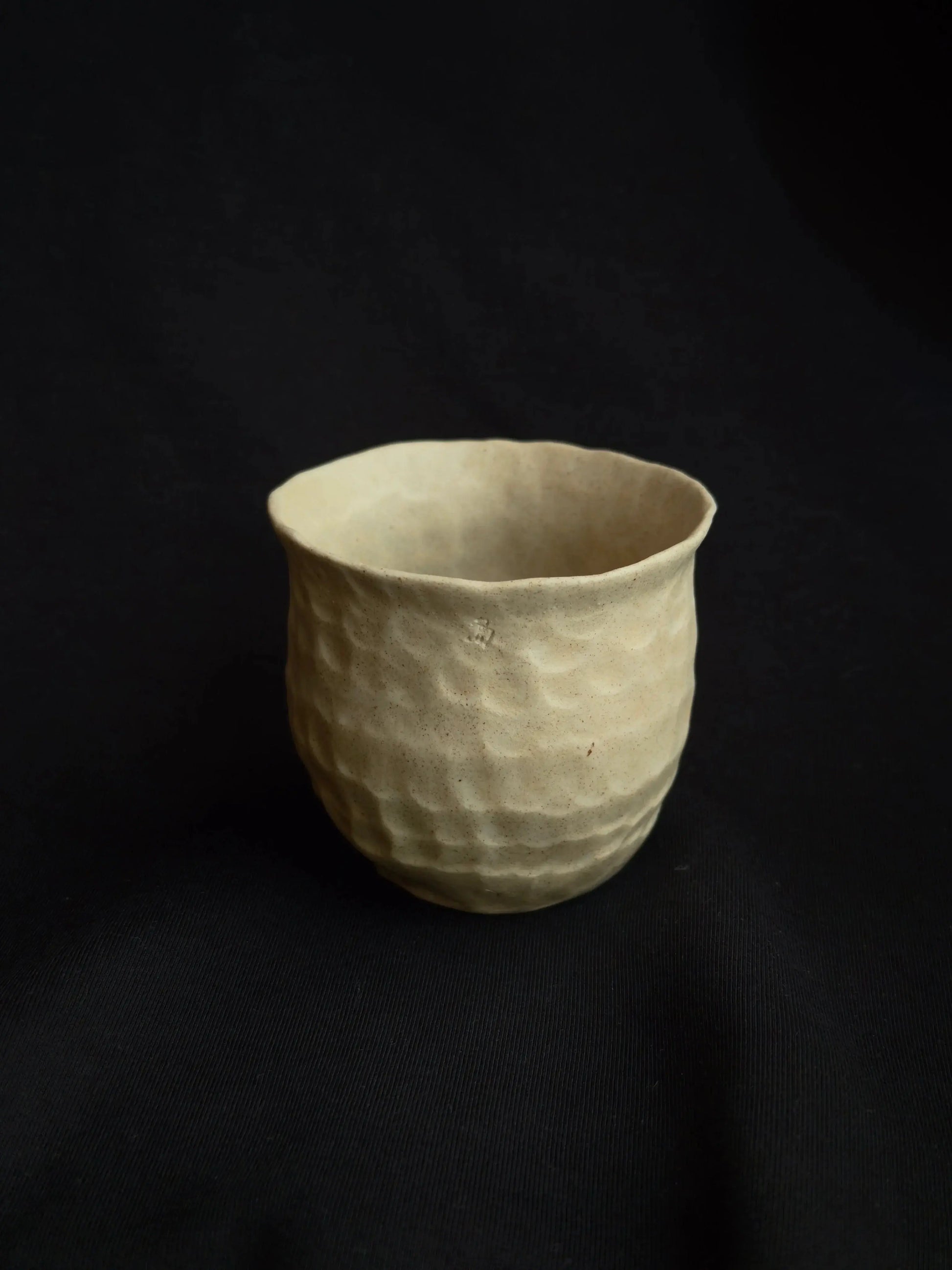 Handcrafted beige ceramic cup with textured surface on a black background