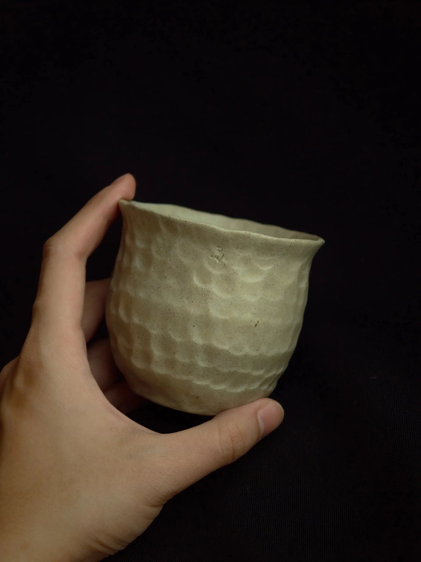 Hand holding a textured, handcrafted ceramic cup against a dark background