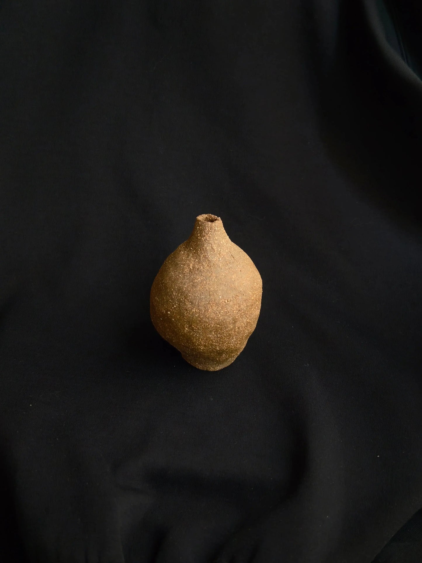 Handcrafted textured ceramic vase on black fabric background, minimalistic decor
