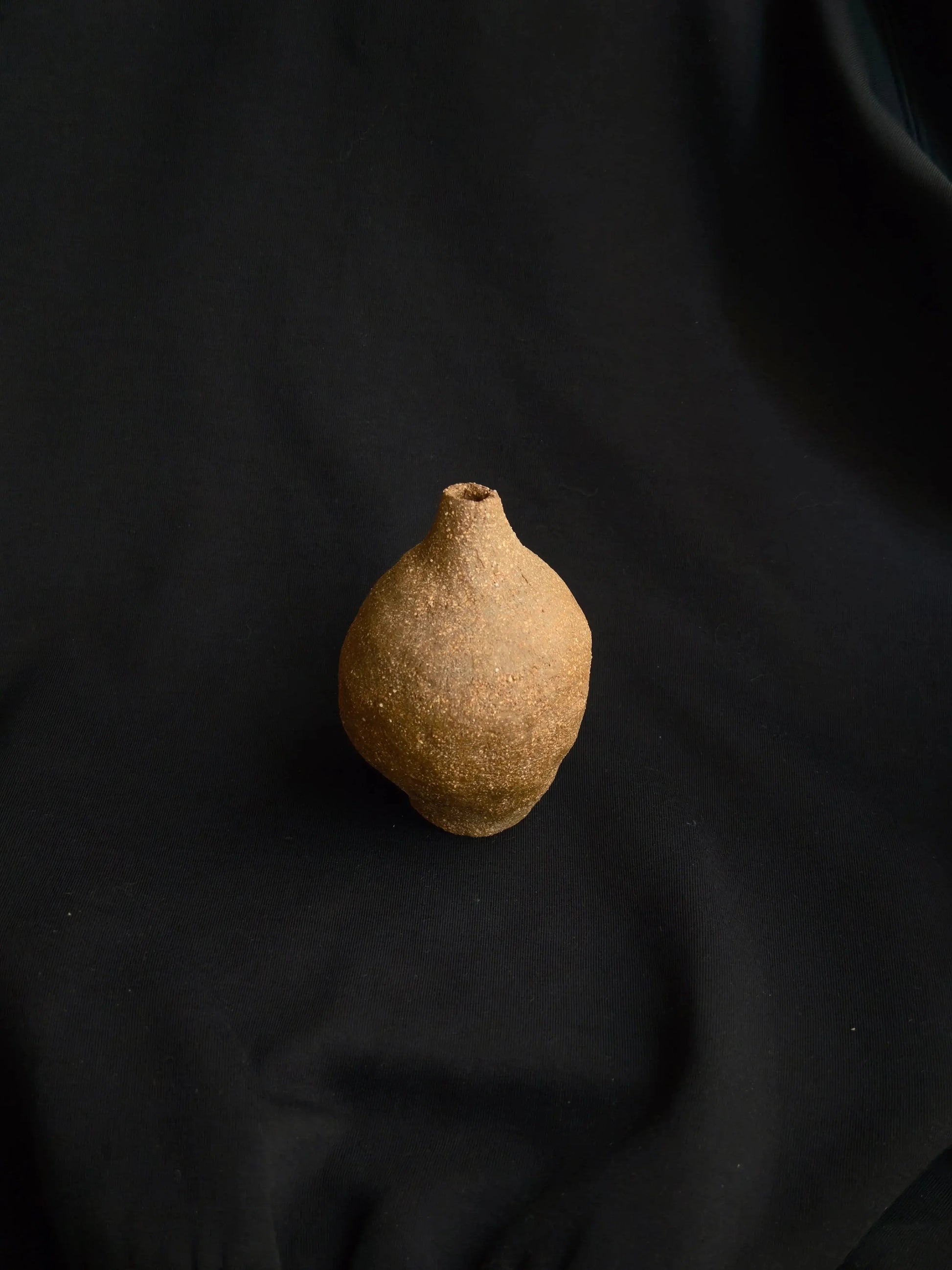 Handcrafted textured ceramic vase on black fabric background, minimalistic decor