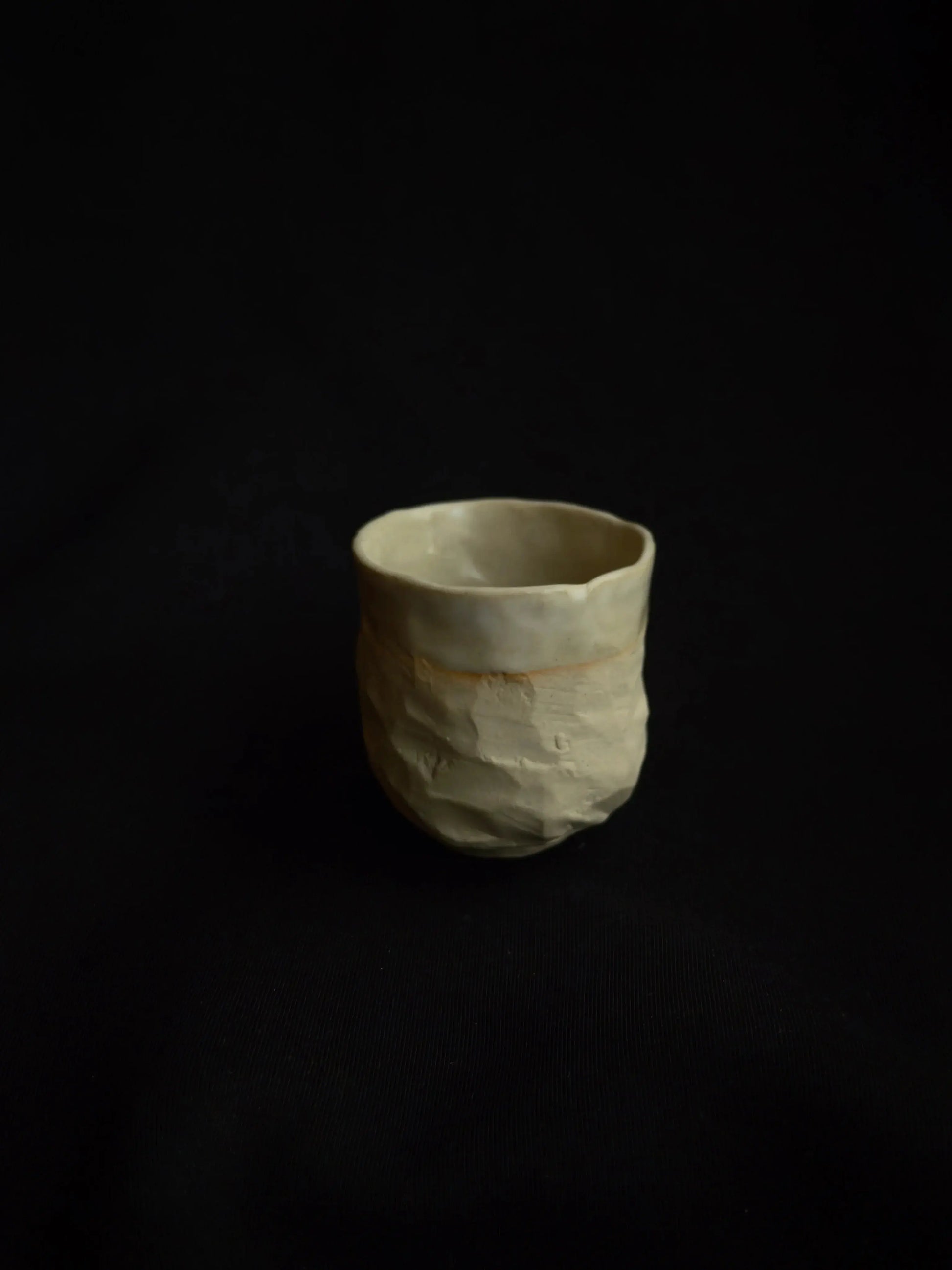 Handcrafted ceramic cup with a textured, minimal design on a black background