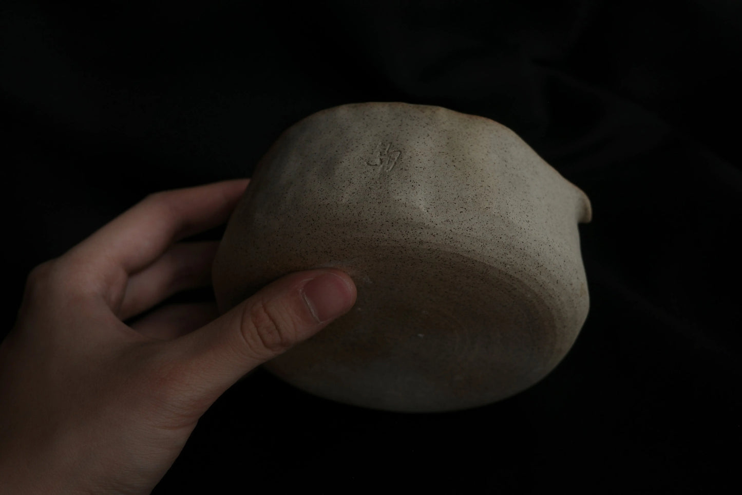 Hand holding a minimalist handcrafted ceramic bowl with a natural matte finish on a black background