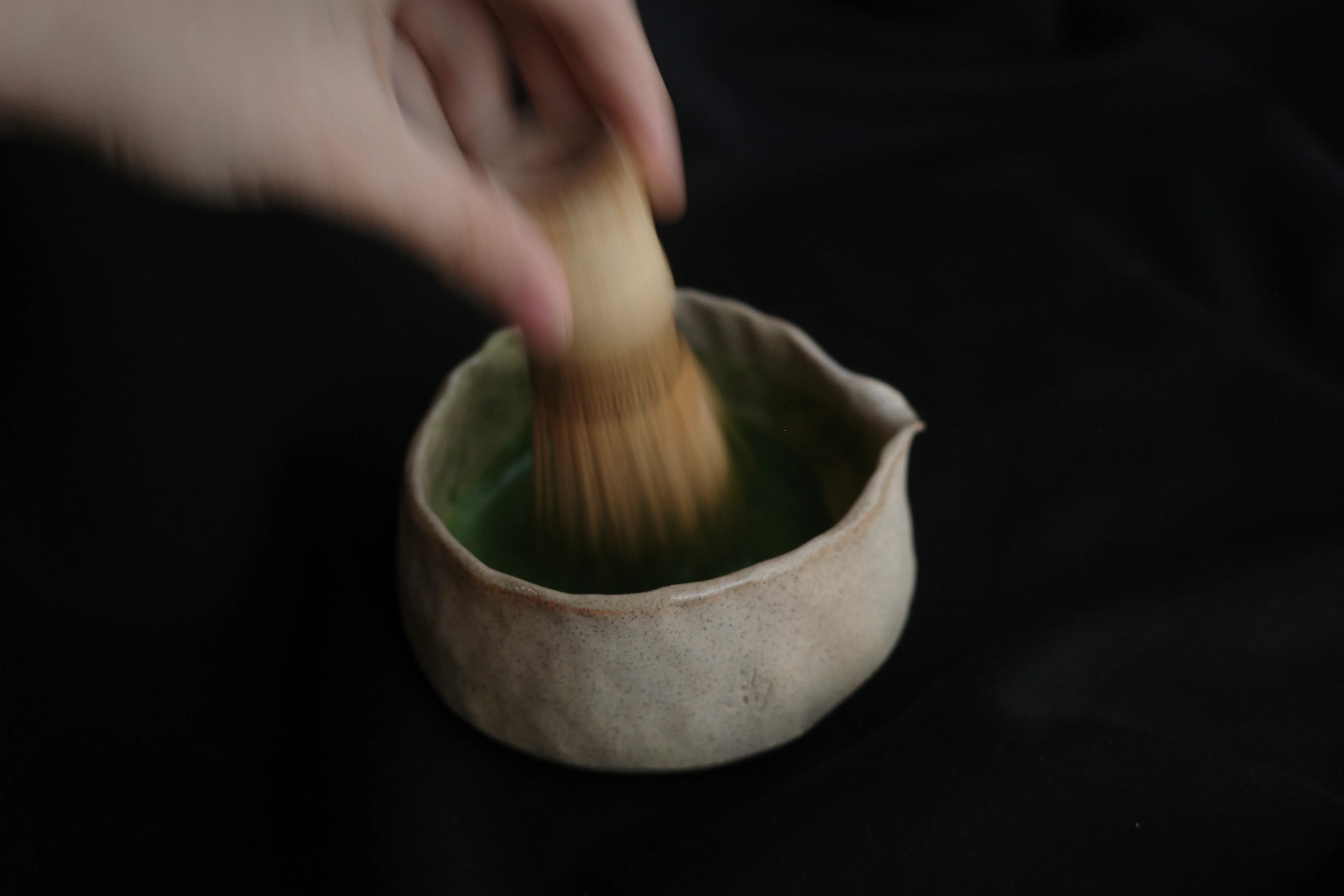 Handcrafted ceramic matcha bowl with bamboo whisk on black background