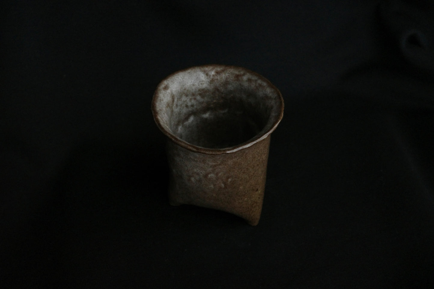 Handcrafted ceramic cup with earthy glaze on a dark background