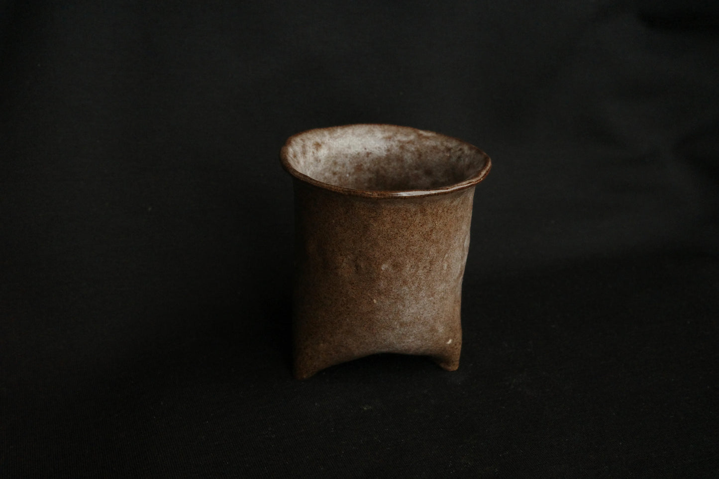 Handcrafted brown ceramic cup with a textured, minimalist design on a dark background