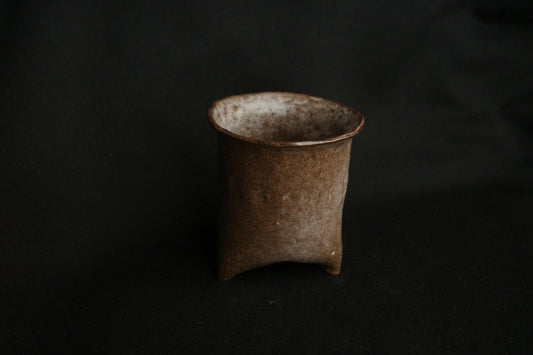 Handcrafted brown ceramic cup with a textured, minimalist design on a dark background