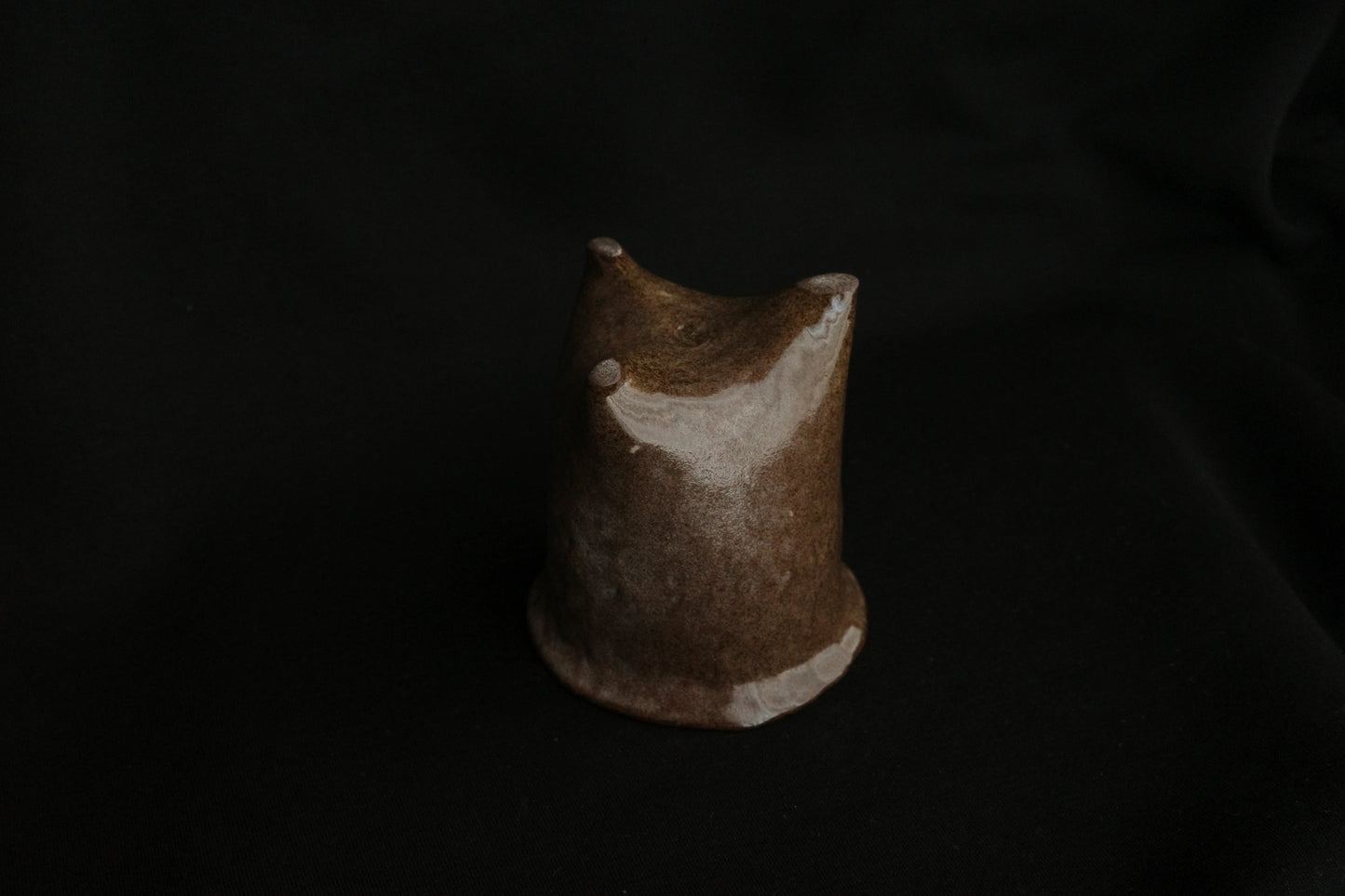 Handcrafted brown ceramic cup with unique sculpted form on a black background