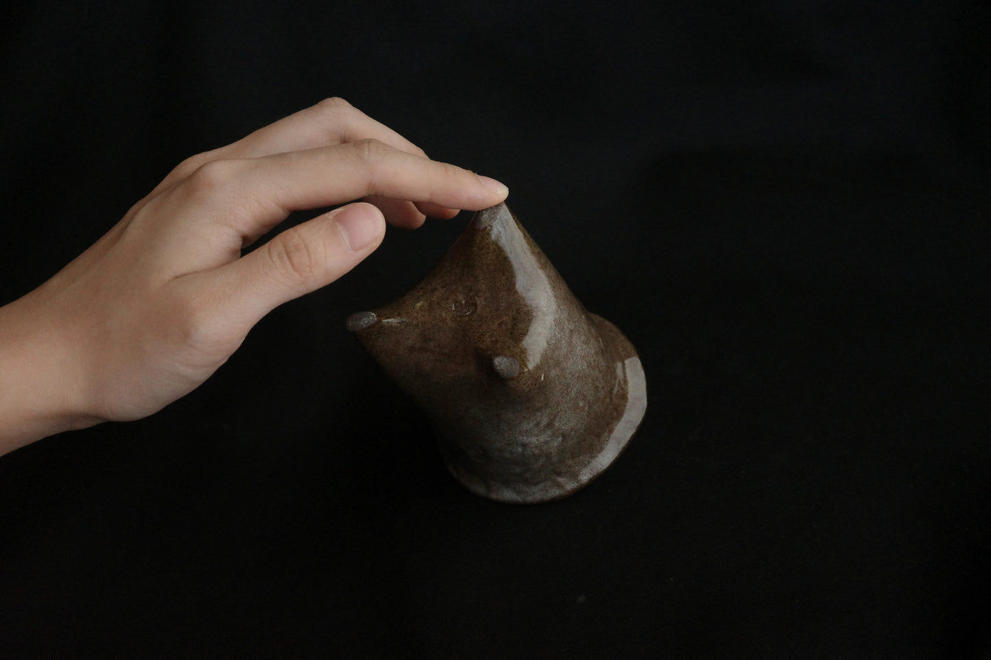 Hand touching handcrafted brown ceramic animal sculpture on black background