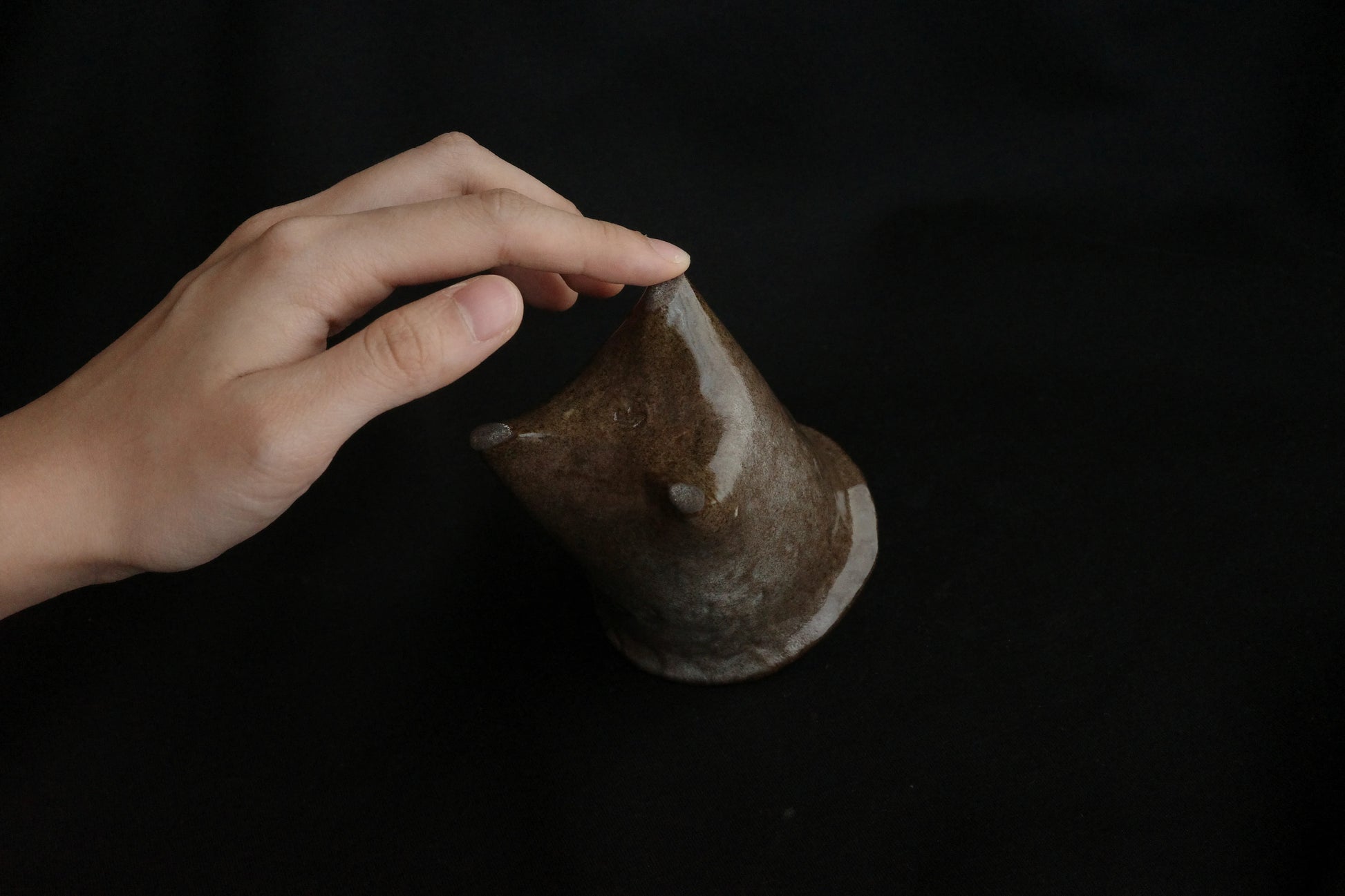 Hand touching handcrafted brown ceramic animal sculpture on black background