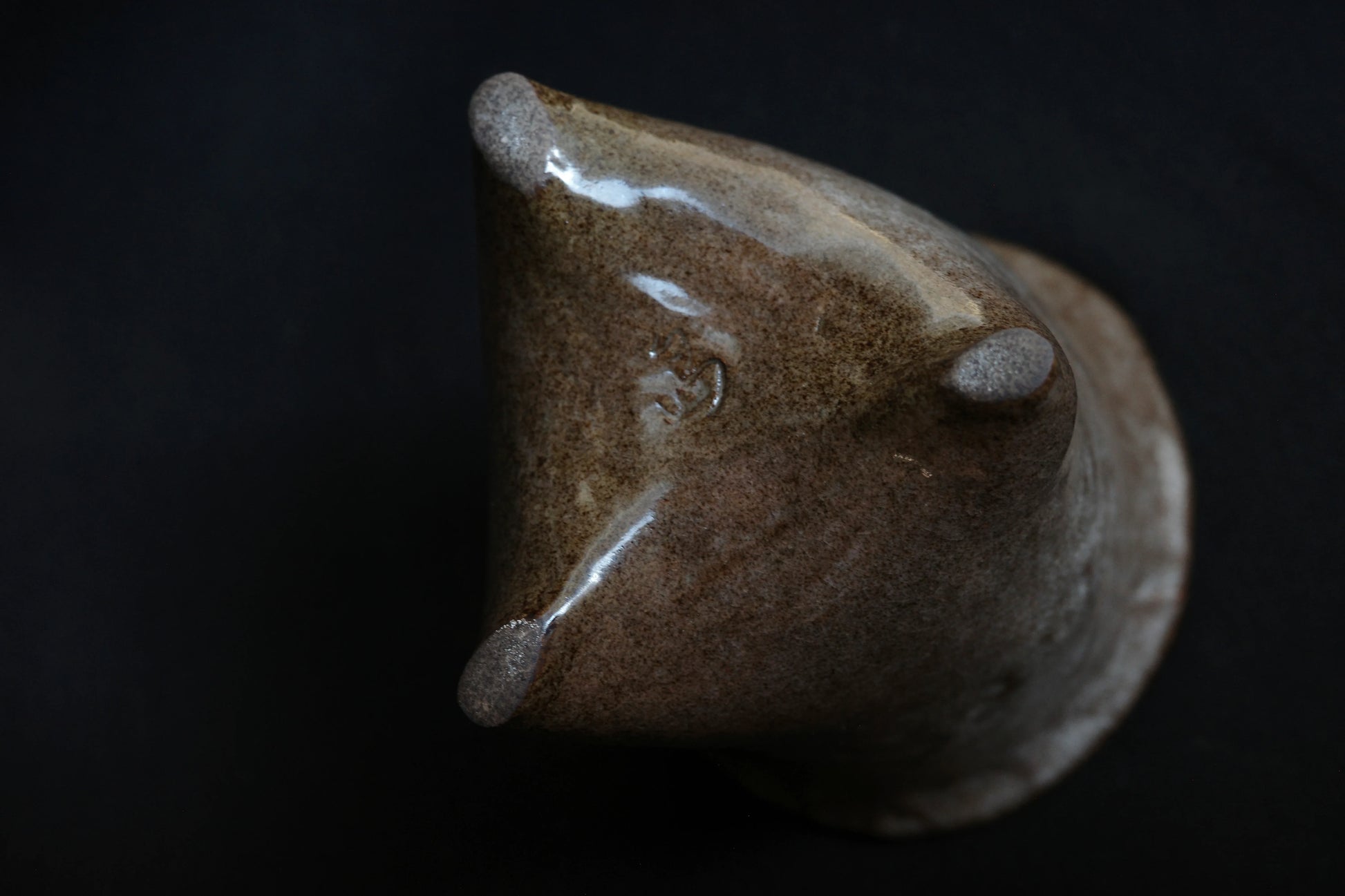 Handcrafted brown ceramic cup with three pointed tips on a dark background