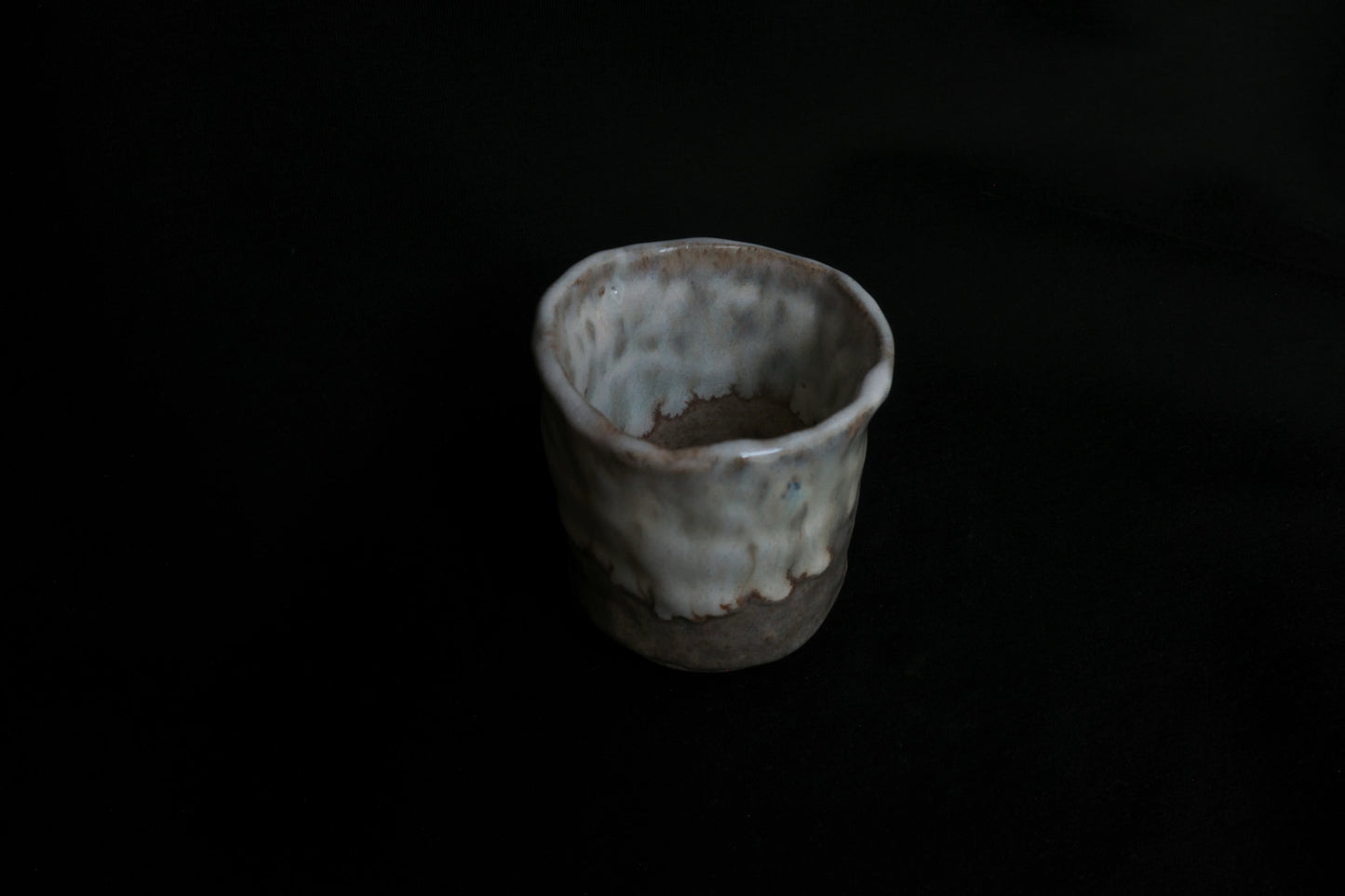Handcrafted ceramic cup with a textured, rustic glaze on a dark background