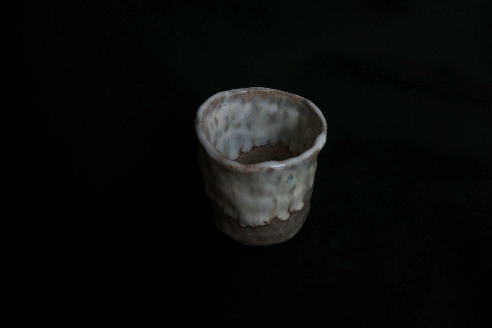 Handcrafted ceramic cup with a textured, rustic glaze on a dark background