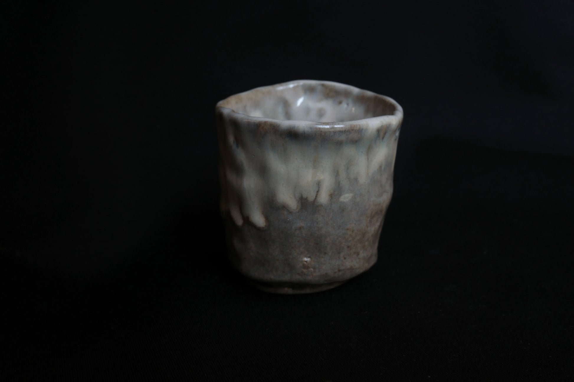 Handcrafted ceramic cup with organic shape and glossy, dripped glaze on dark background