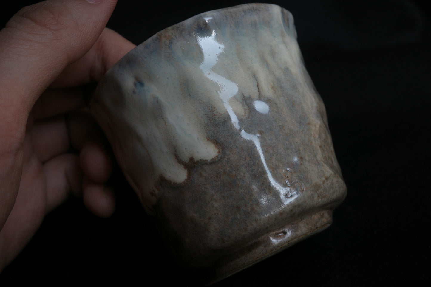 Hand holding a handcrafted ceramic cup with a natural, minimalist glaze on a dark background