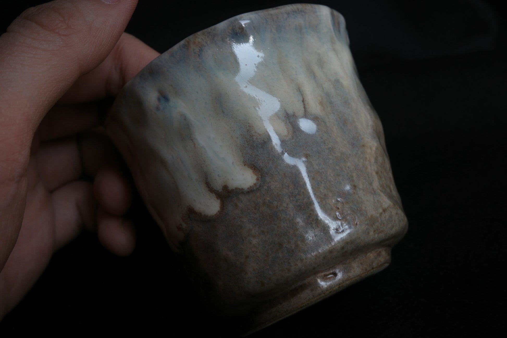 Hand holding a handcrafted ceramic cup with a natural, minimalist glaze on a dark background