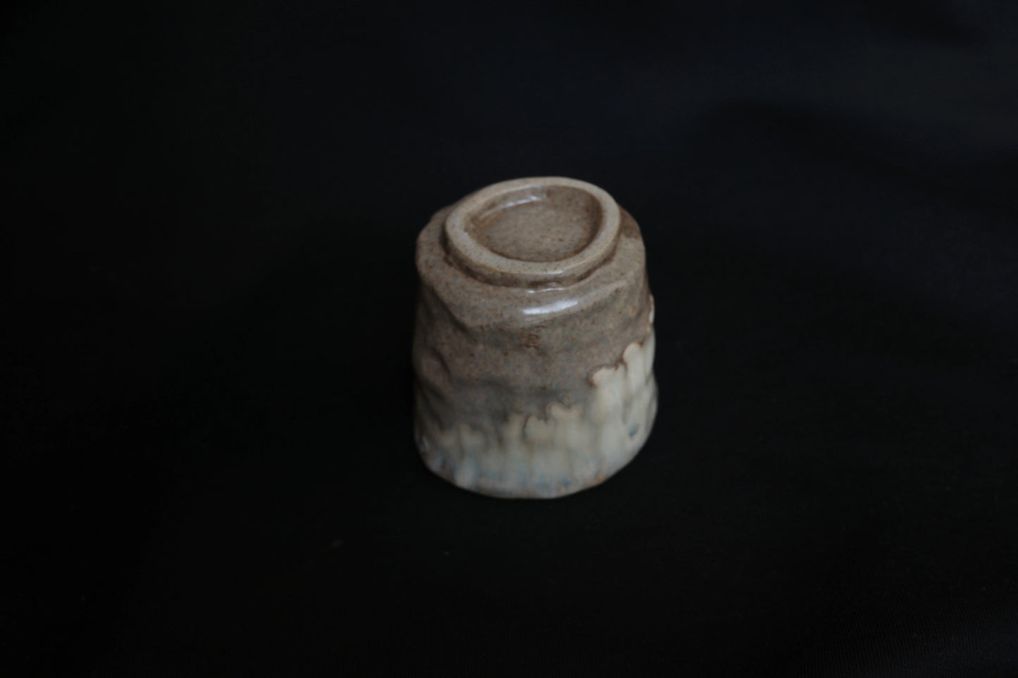 Handcrafted ceramic cup upside down, earth-toned glaze, minimalist style, black background