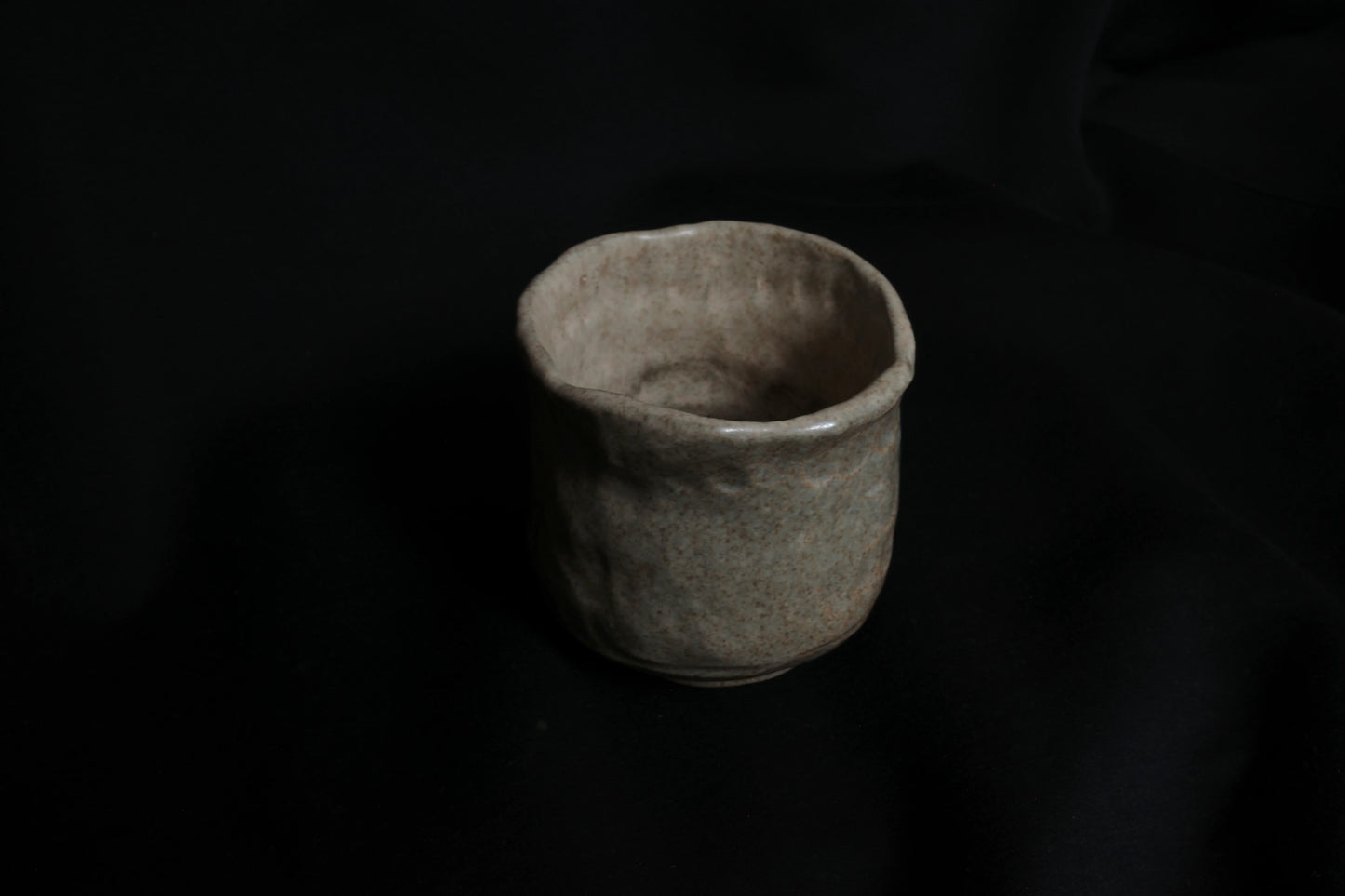 Handcrafted ceramic cup with organic shape on a dark background, minimalist pottery
