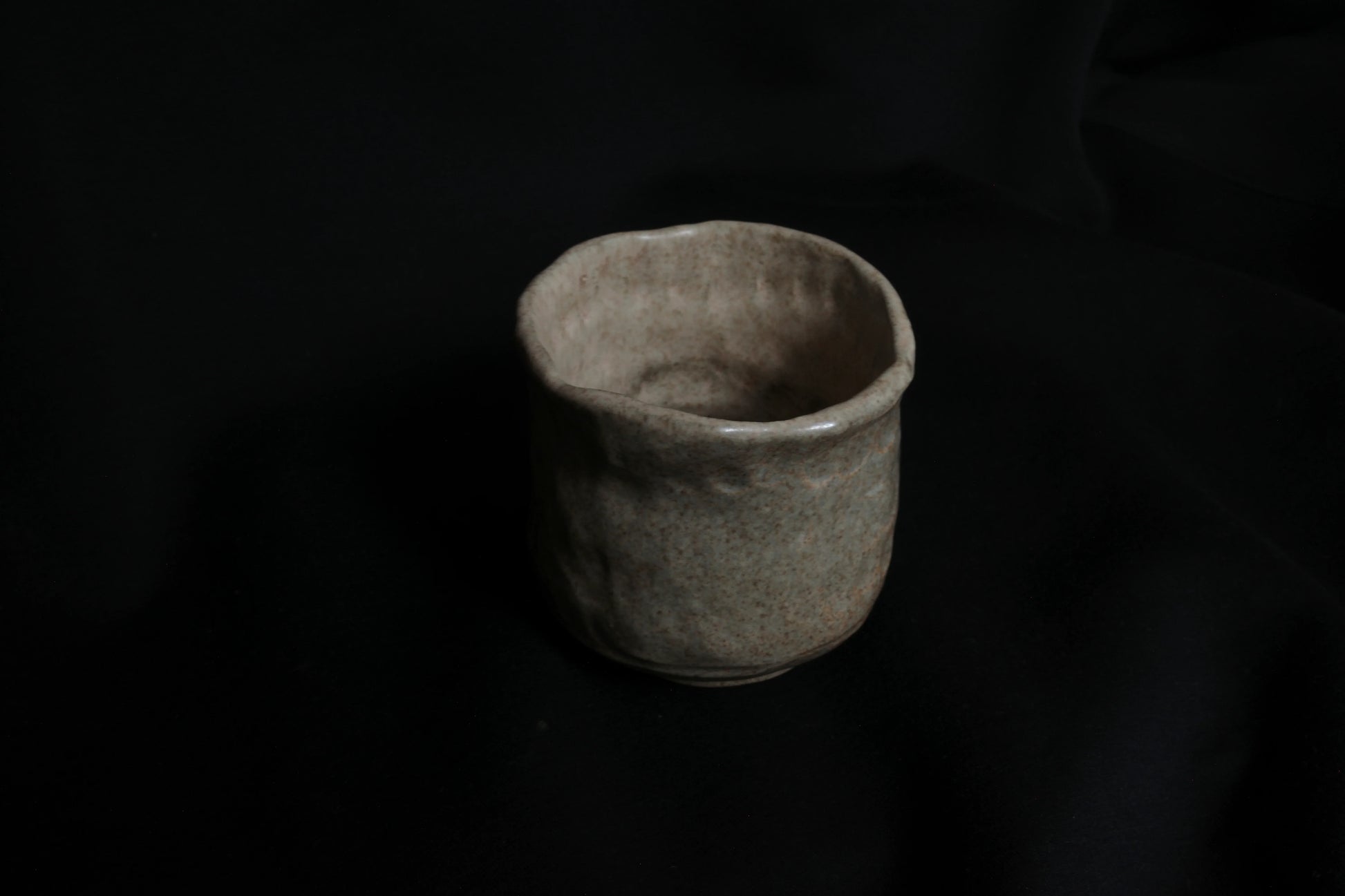 Handcrafted ceramic cup with organic shape on a dark background, minimalist pottery
