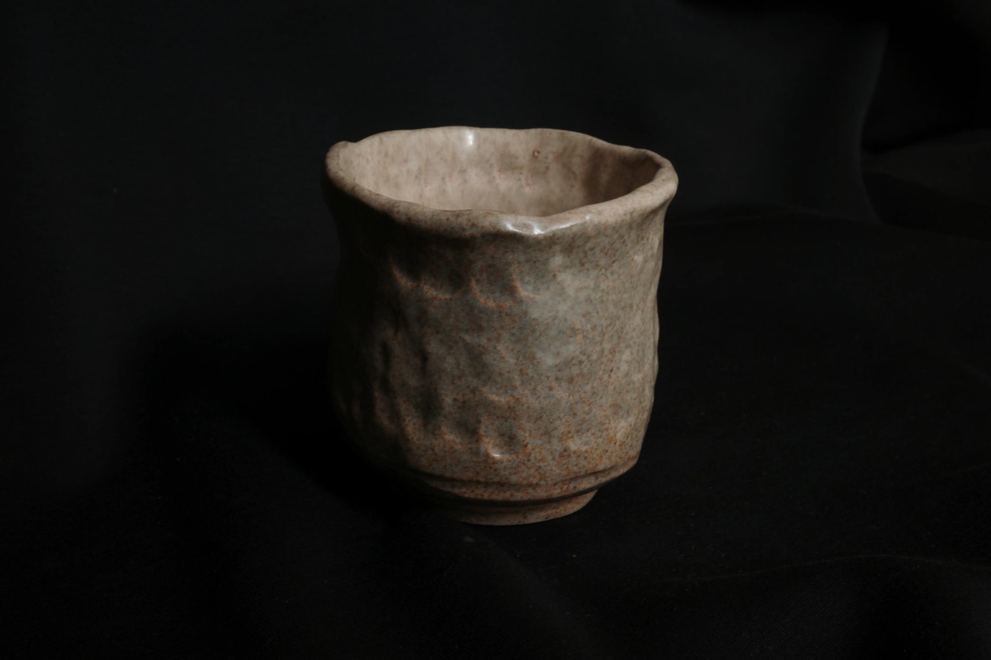 Handcrafted ceramic cup with textured surface on black fabric background