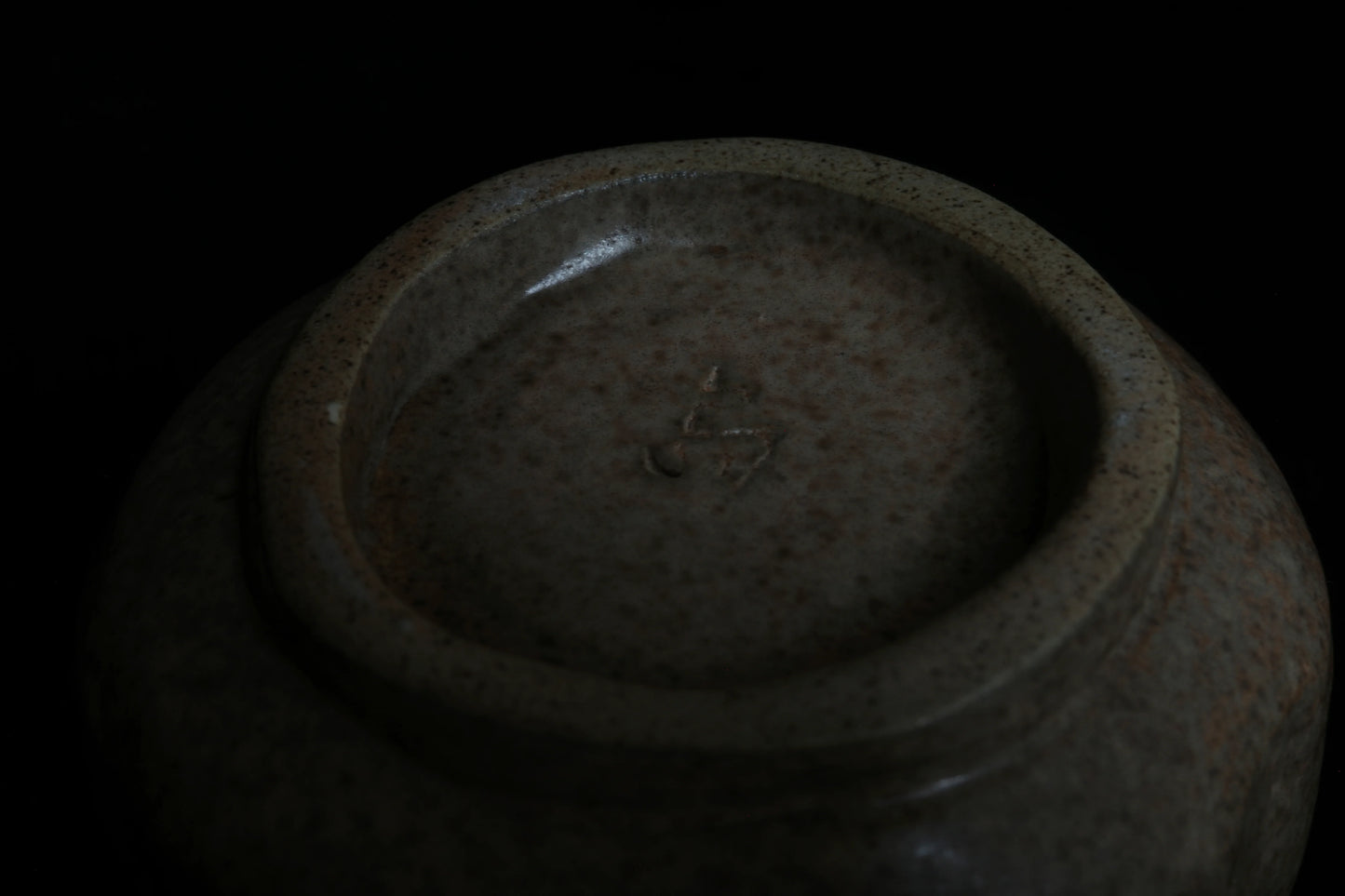 Close-up of the base of a handcrafted speckled ceramic bowl with artist’s mark, minimal style