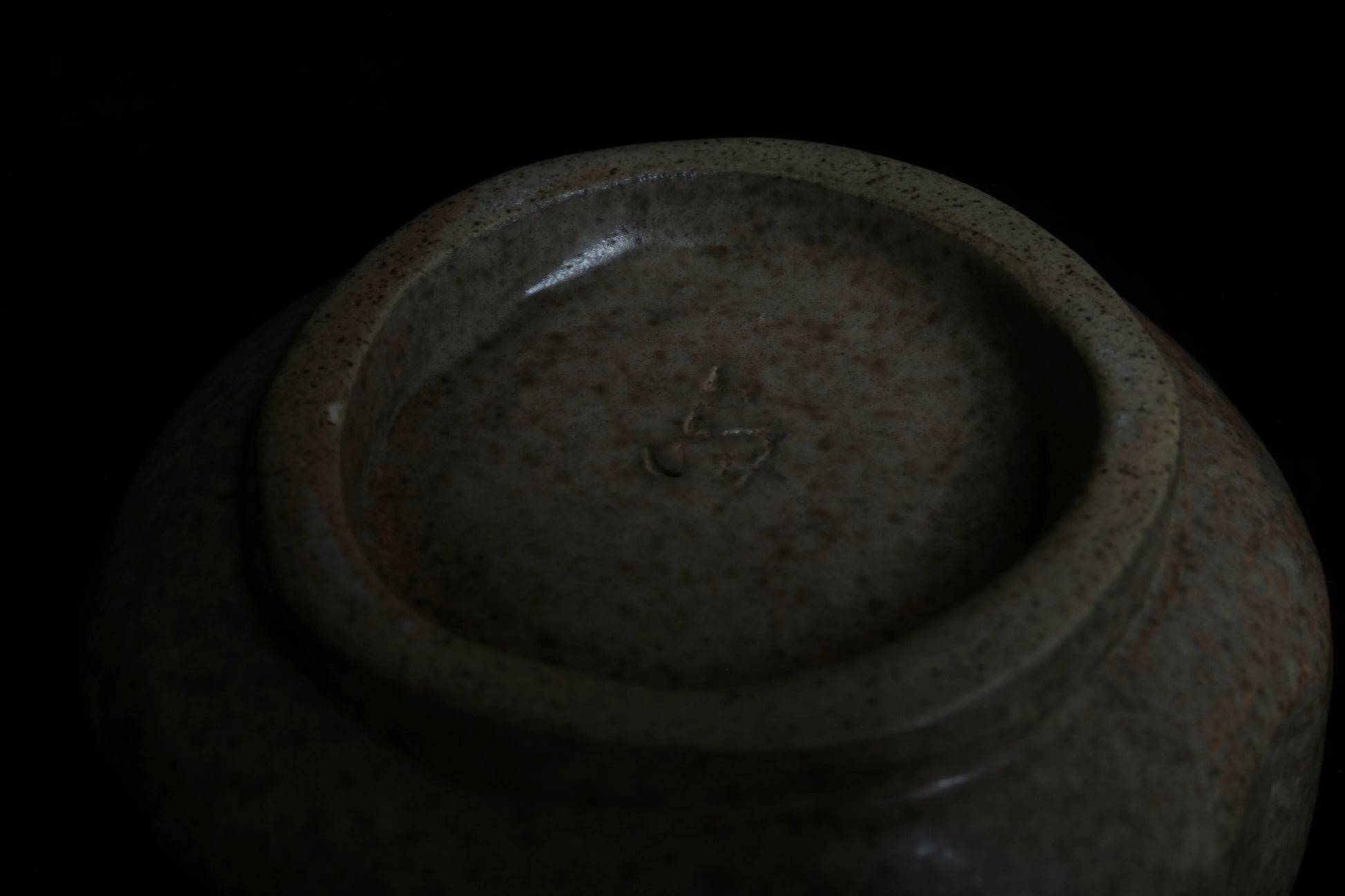 Close-up of the base of a handcrafted speckled ceramic bowl with artist’s mark, minimal style