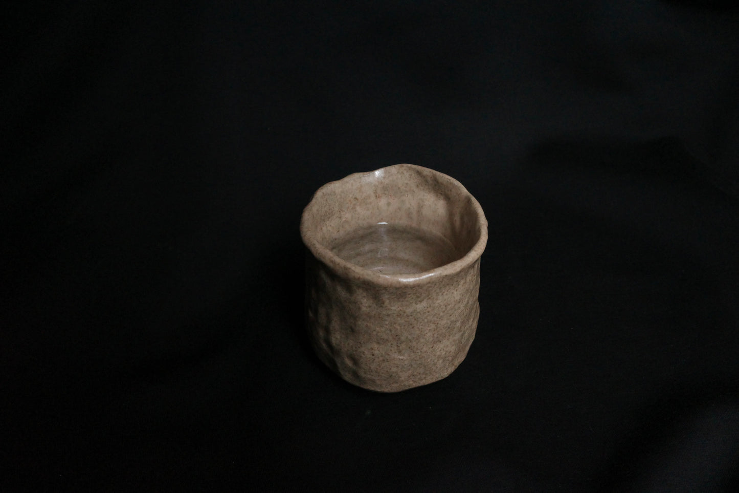 Handcrafted ceramic cup with a natural beige glaze on a black background