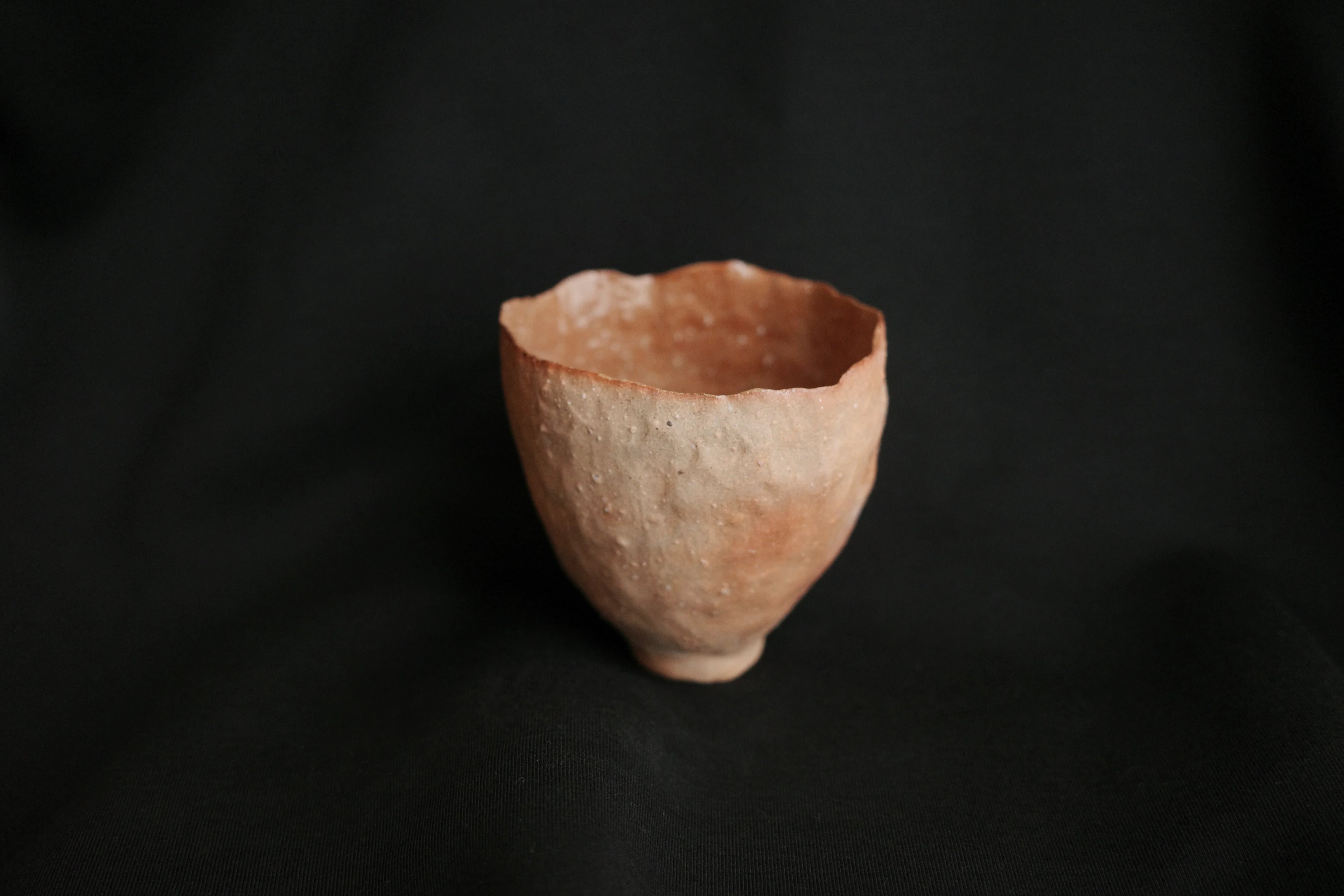 Handcrafted ceramic cup with organic texture on black background, minimalist style
