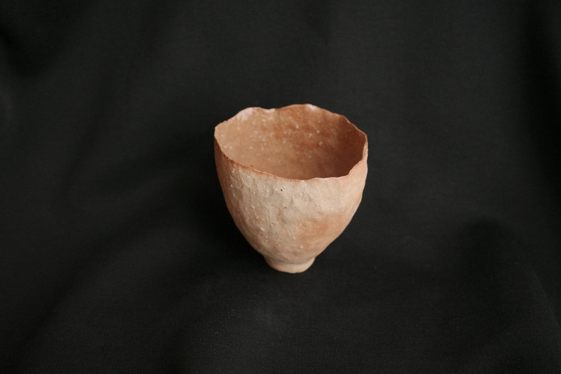 Handcrafted minimalist ceramic cup with organic texture on black background