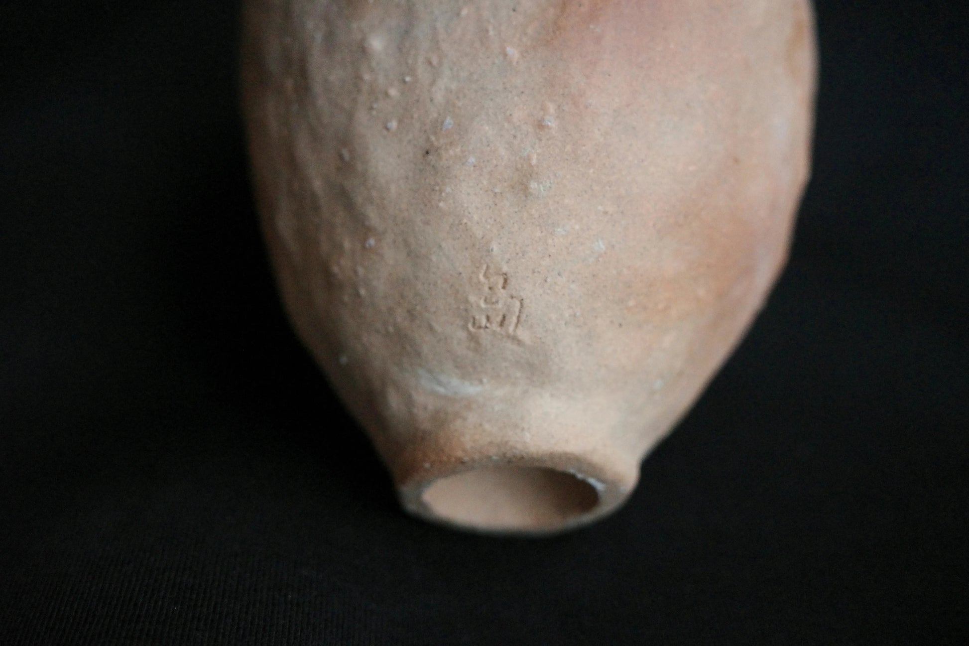 Close-up of handcrafted ceramic vase with natural textured surface and maker’s mark