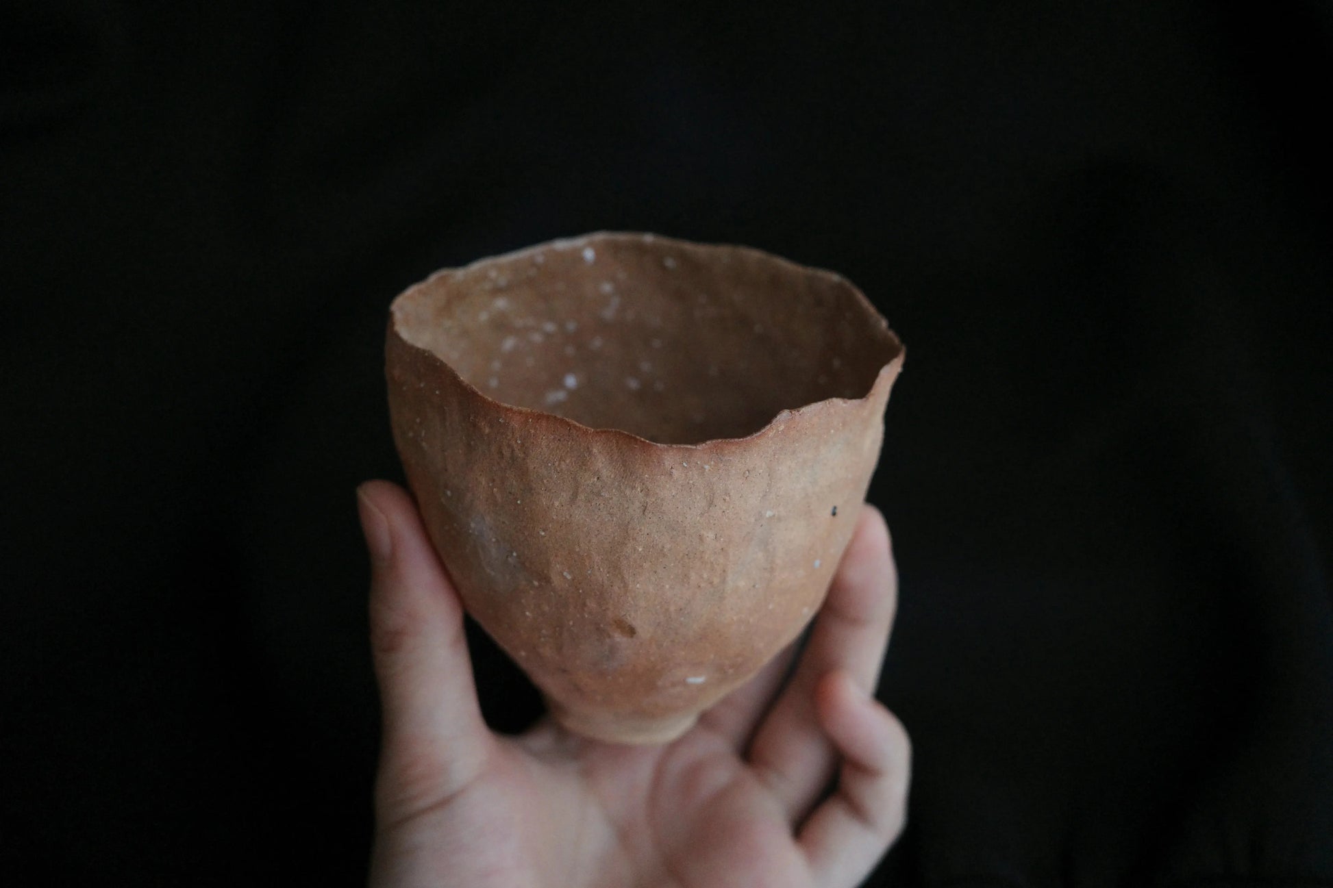 Hand holding a handcrafted, minimalist ceramic cup with a natural, textured finish