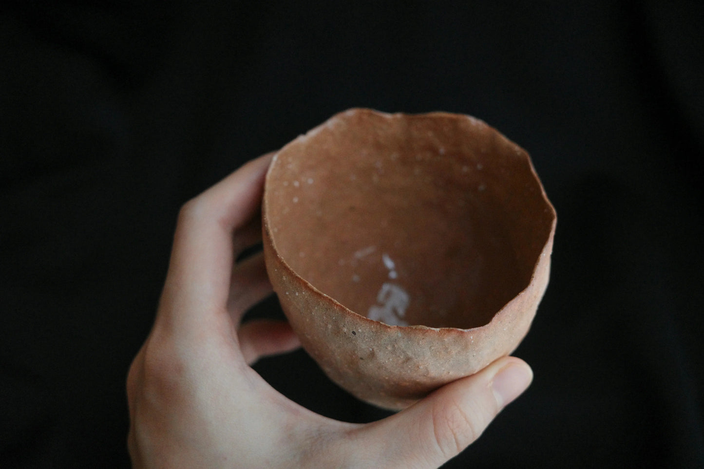 Hand holding a handcrafted, minimalist ceramic bowl with an organic, uneven rim