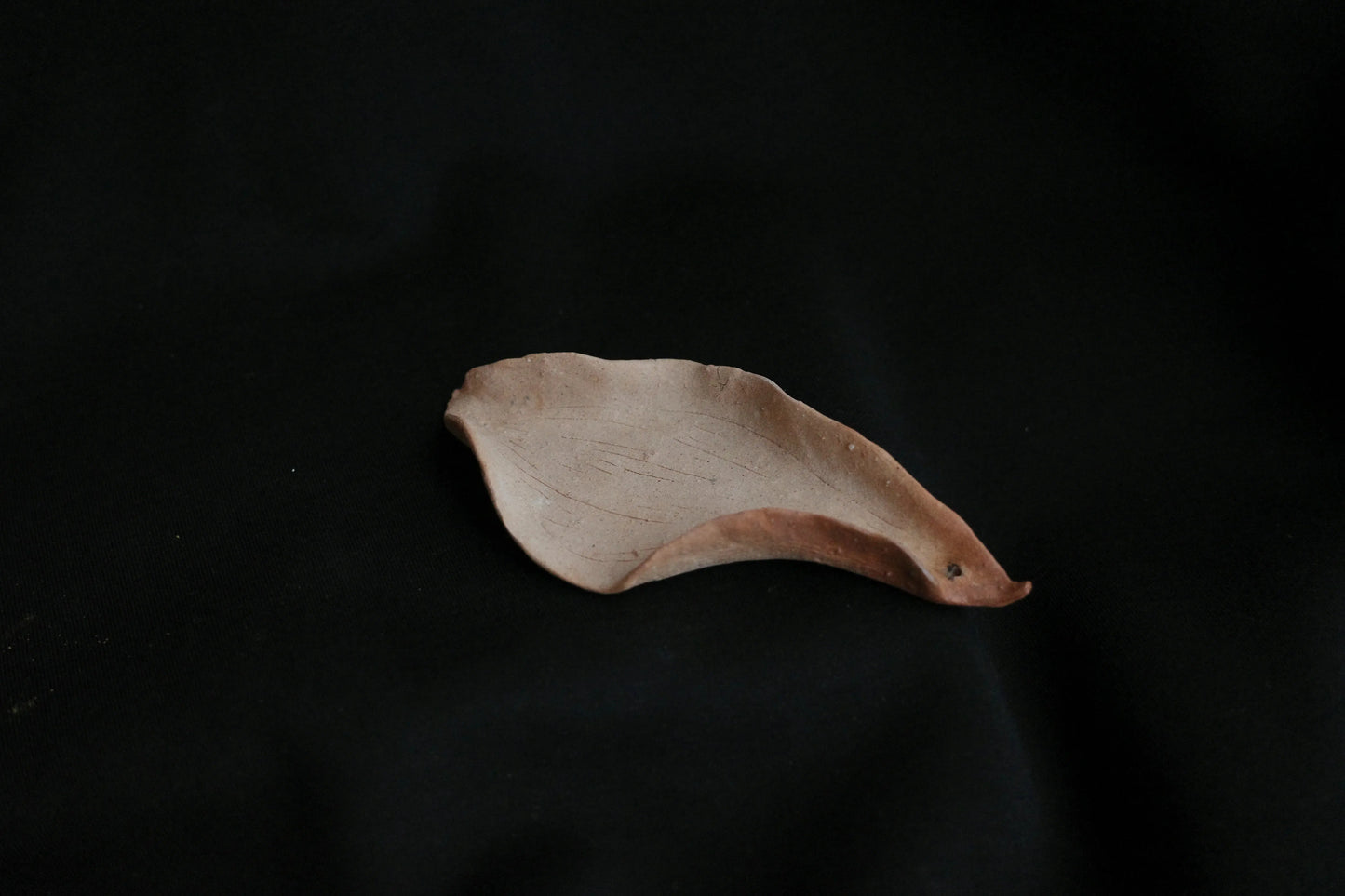 Handcrafted ceramic dish in organic leaf shape on black background, minimalist home decor