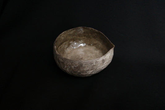 Handcrafted ceramic bowl with rustic, textured finish on a black background
