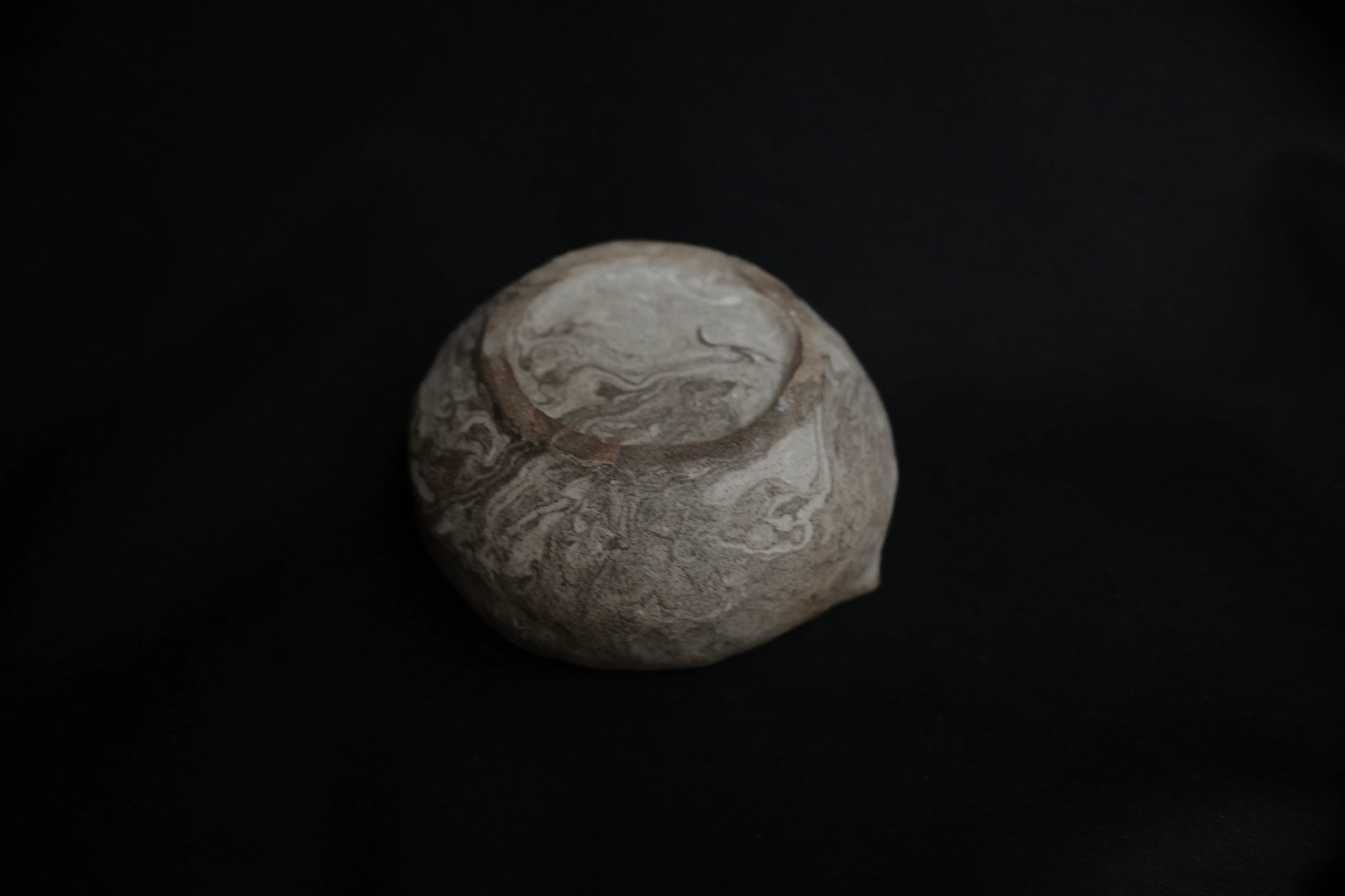 Handcrafted ceramic bowl base with marbled texture on a black background
