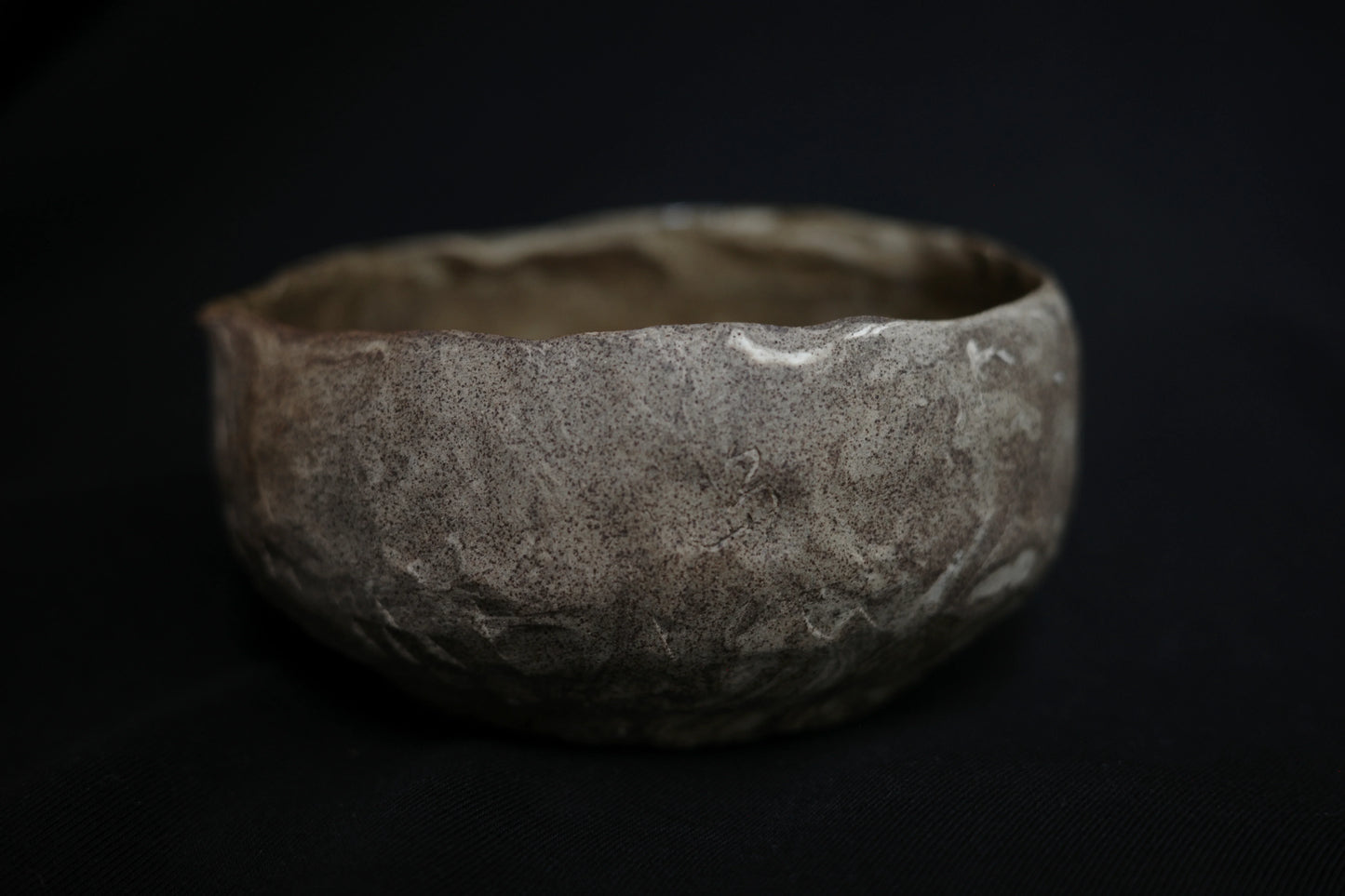 Handcrafted ceramic bowl with textured, natural finish on a dark background