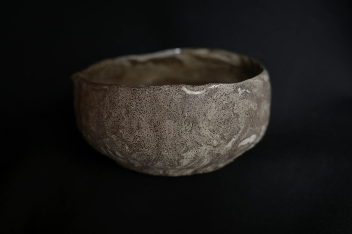 Handcrafted ceramic bowl with textured, natural finish on a dark background