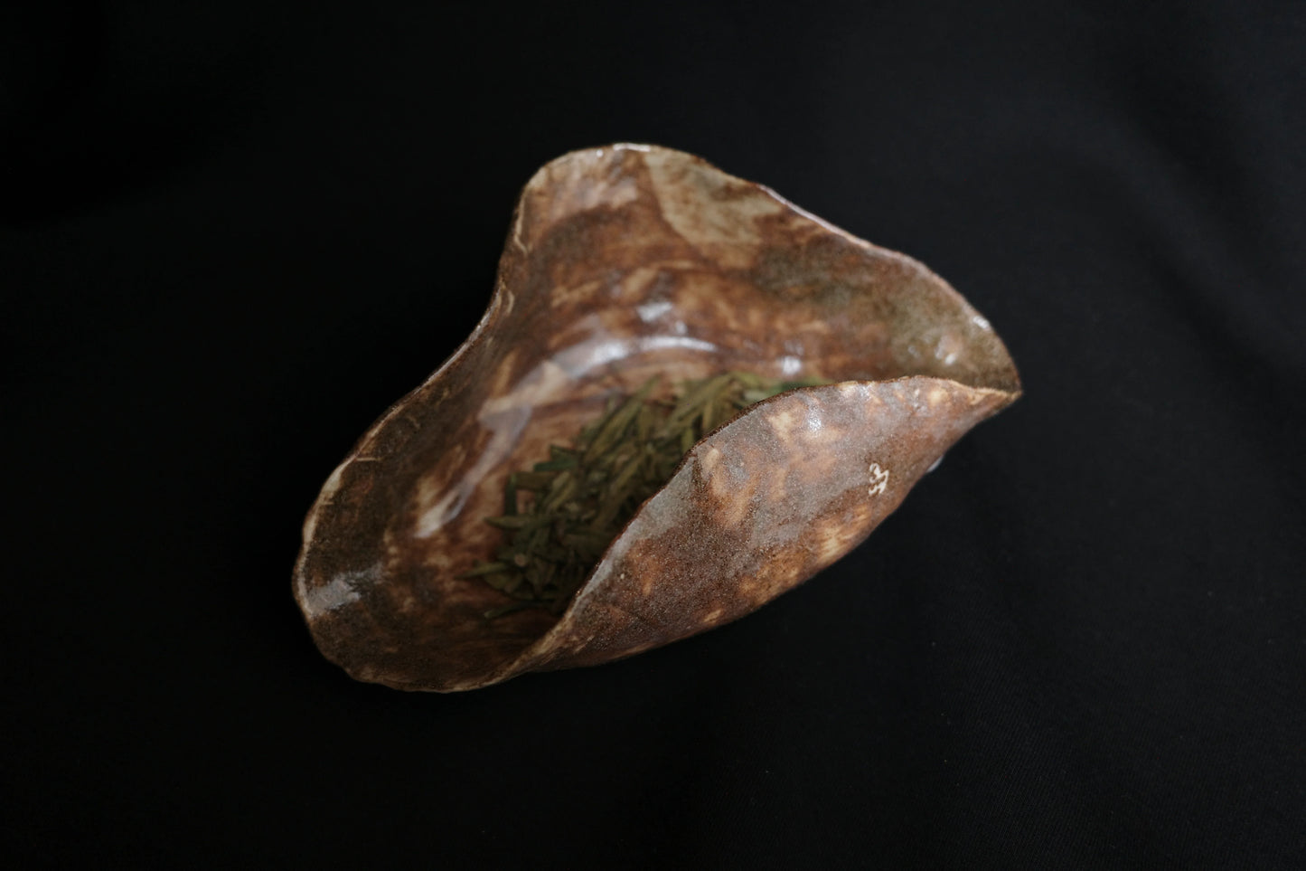 Handcrafted ceramic bowl with organic shape and earthy glaze, holding green tea leaves