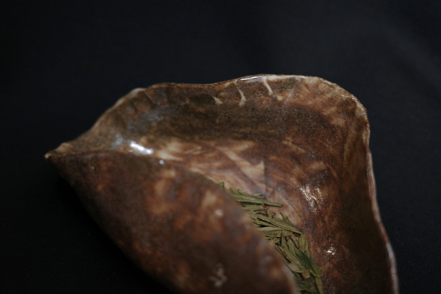 Handcrafted ceramic dish with green tea leaves on a dark background