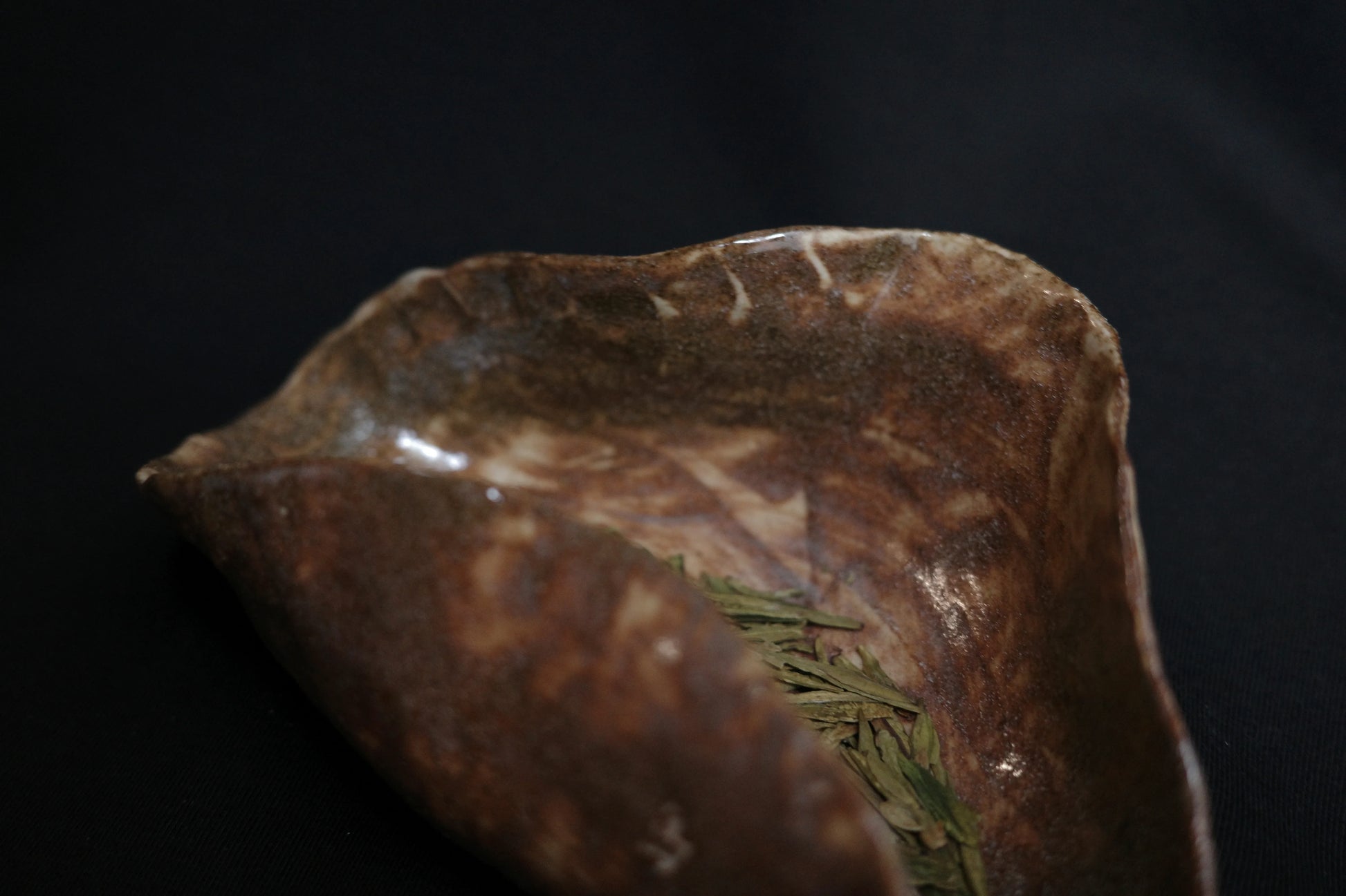 Handcrafted ceramic dish with green tea leaves on a dark background