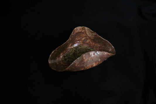 Handcrafted ceramic bowl with organic shape holding loose green tea leaves on black background