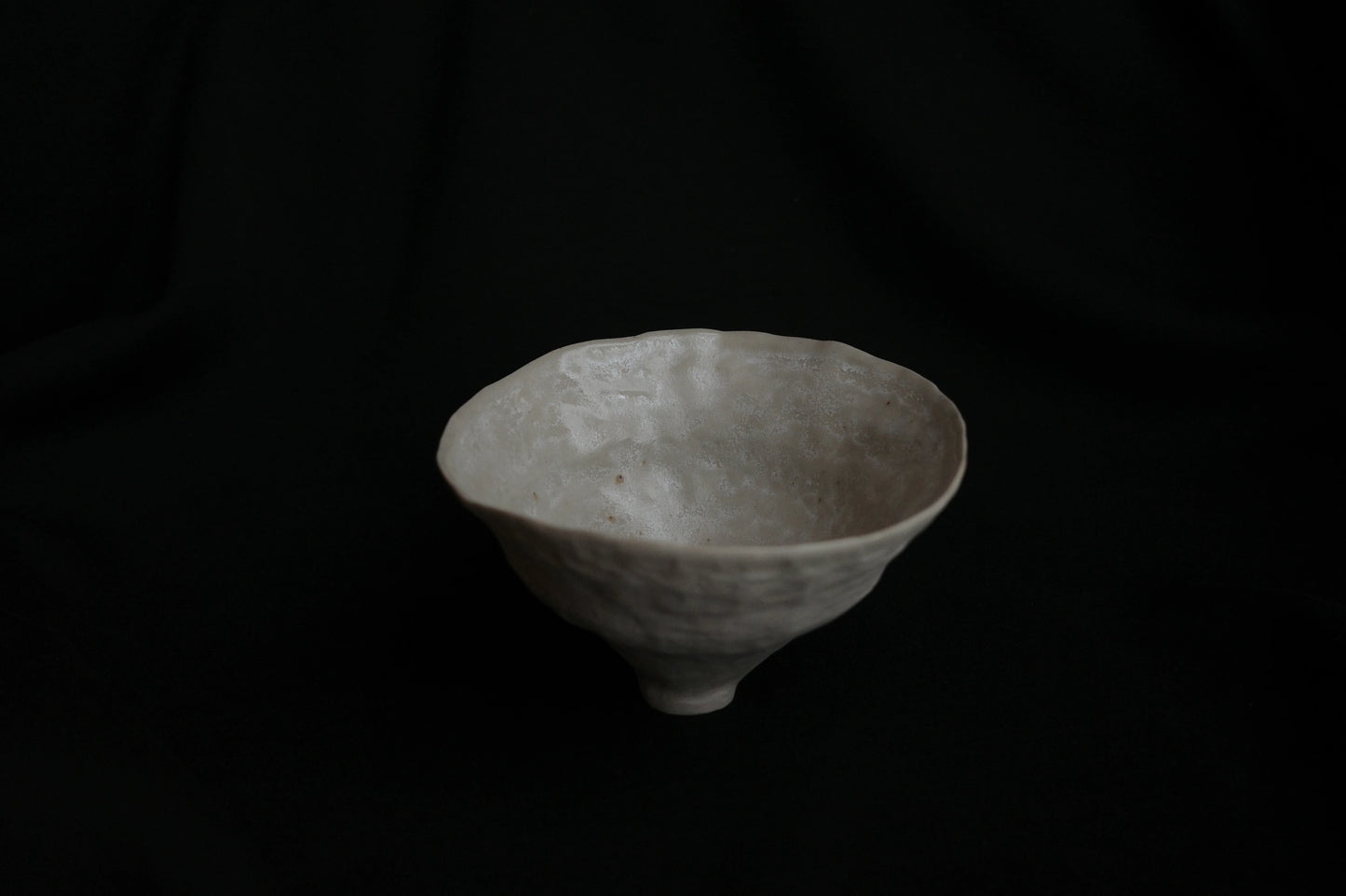 Handcrafted white ceramic bowl with organic texture on a dark background